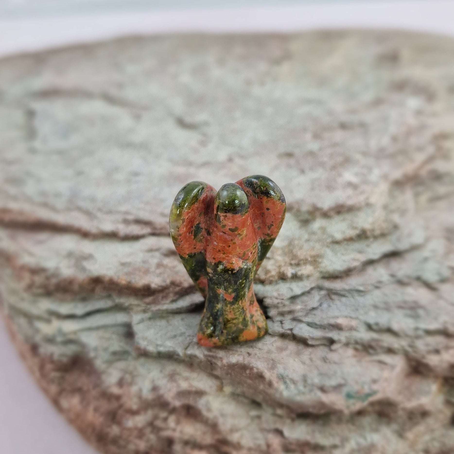 Unakite crystal pocket angel on a rock surface with a blurred background