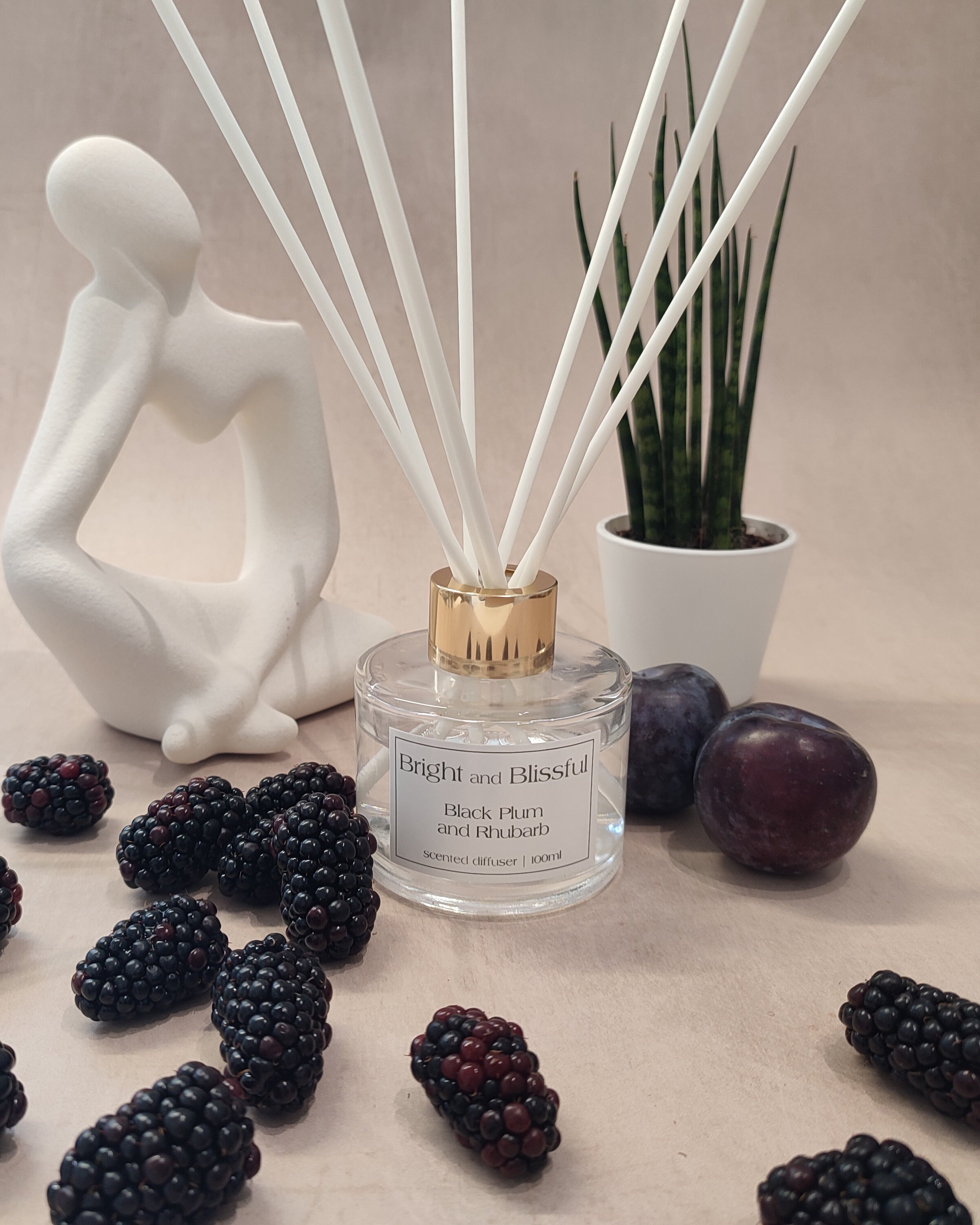 Reed diffuser with black plums and a decorative figure on a neutral background