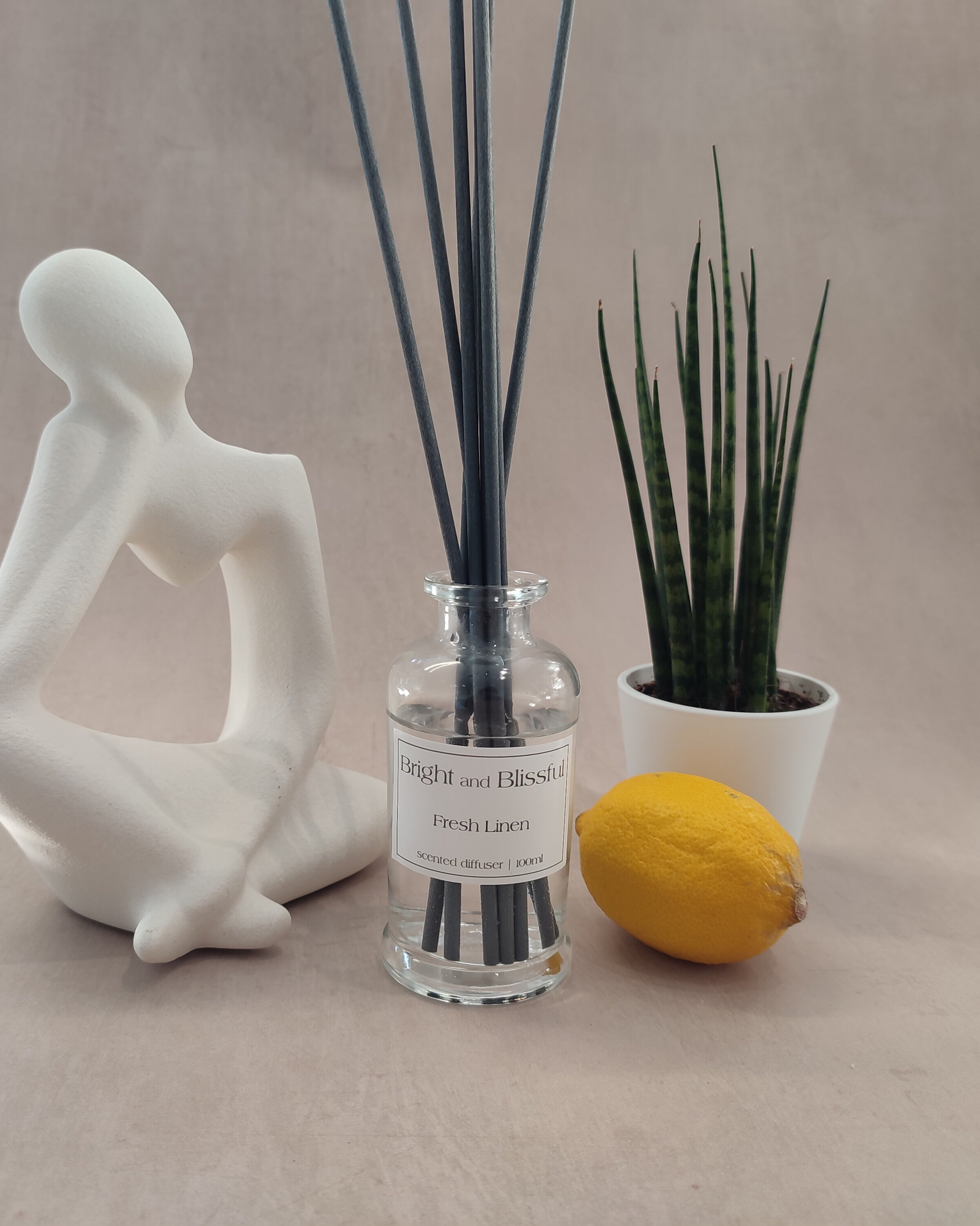 Diffuser bottle with reeds, lemon, and plant on a neutral background
