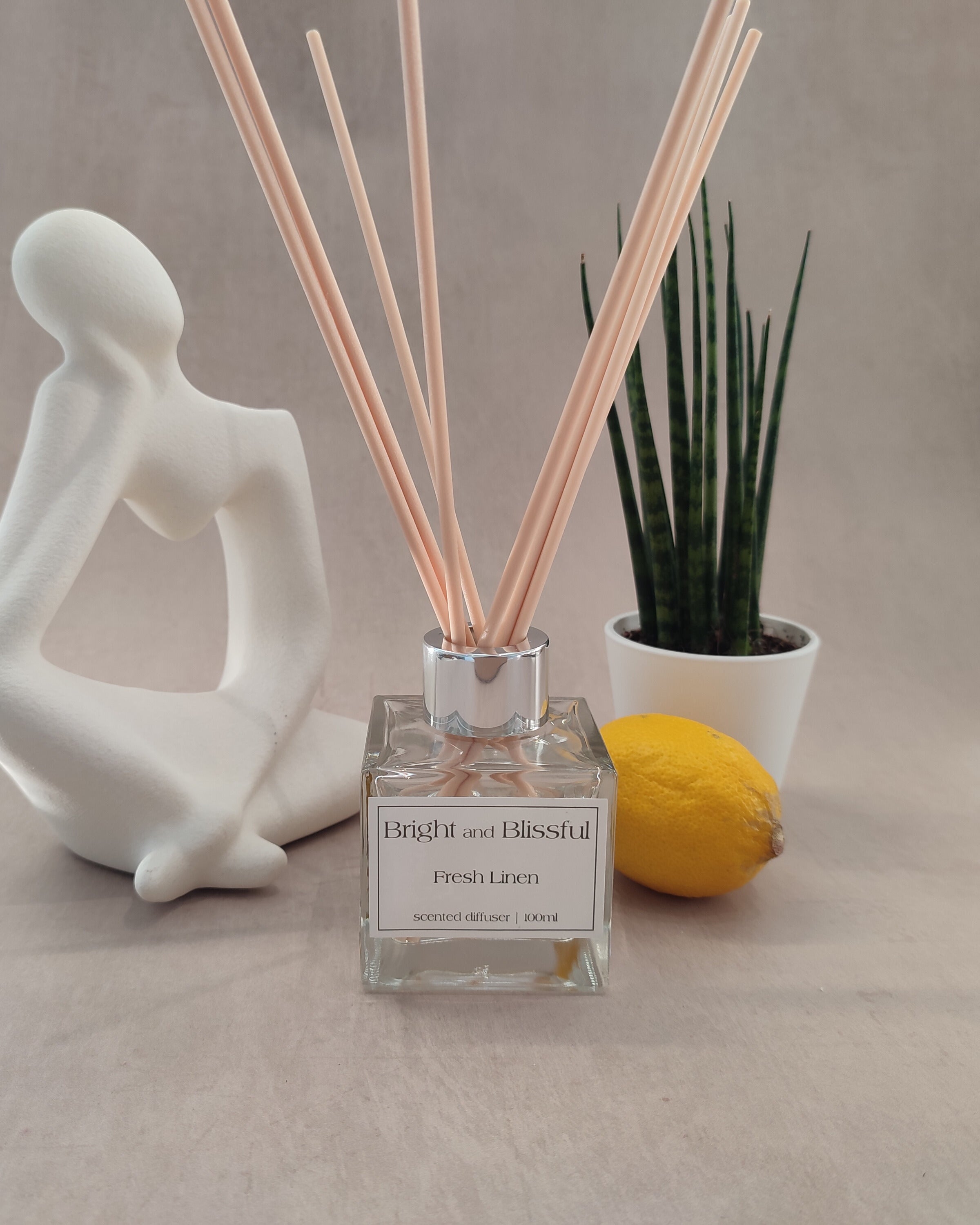 Diffuser with reeds, decorative statue, plant, and lemon on a neutral background