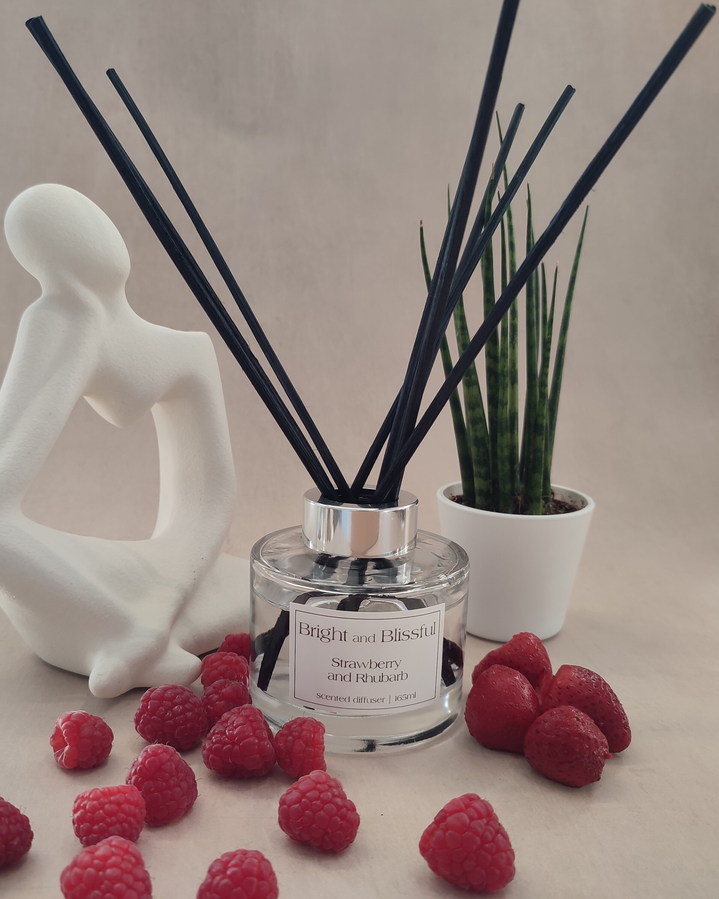 Aromatherapy diffuser with reeds, raspberries, and a decorative figure on a neutral background