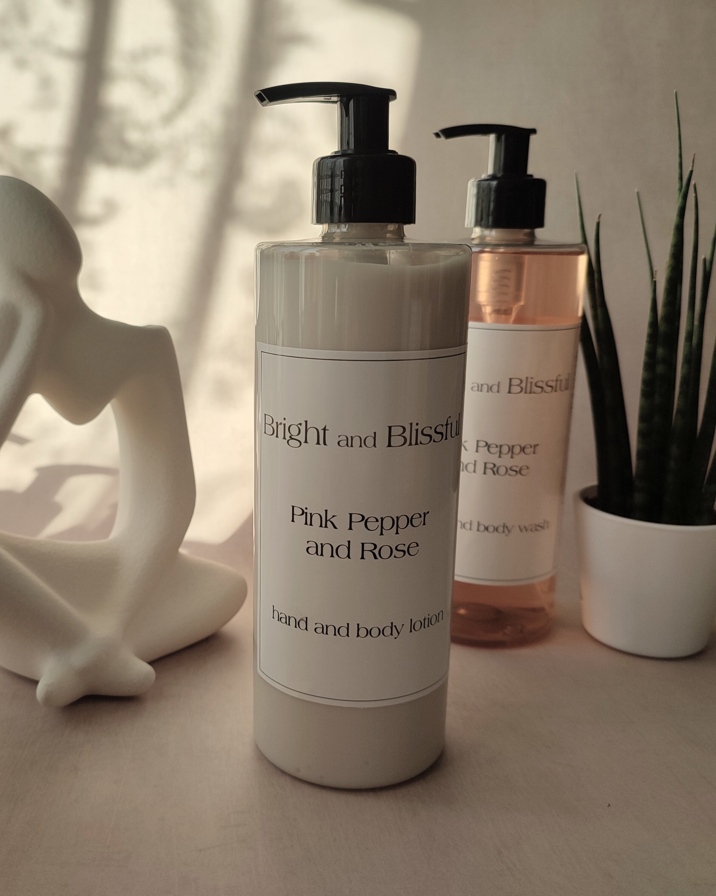 Two bottles of 'Bright and Blissful' body wash on a surface with a plant and sculpture in the background.