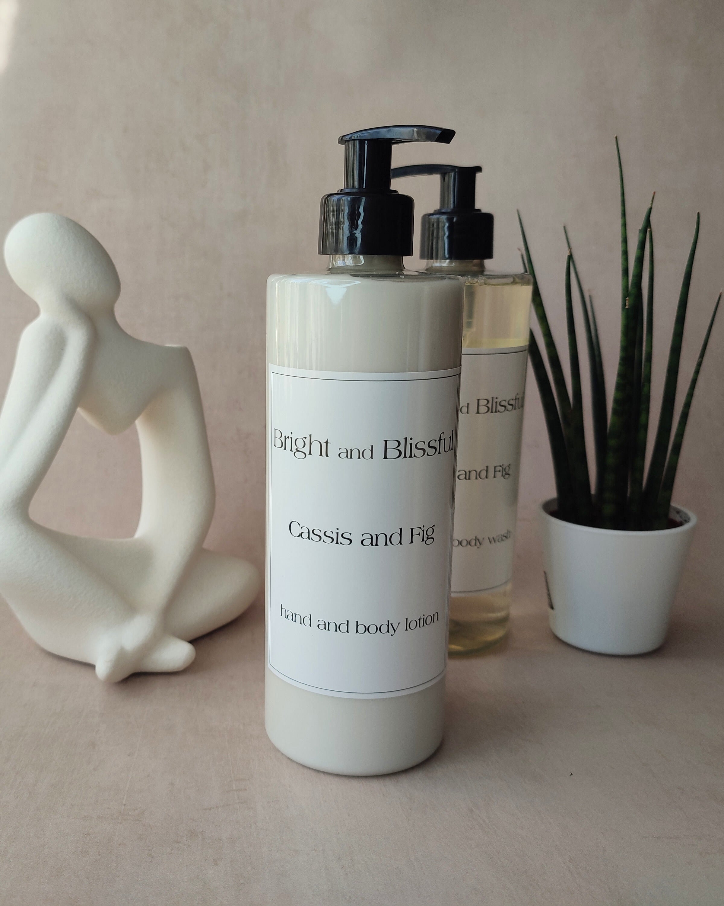 Two bottles of 'Bright and Blissful' hand and body lotion on a neutral background with a decorative statue and plant.