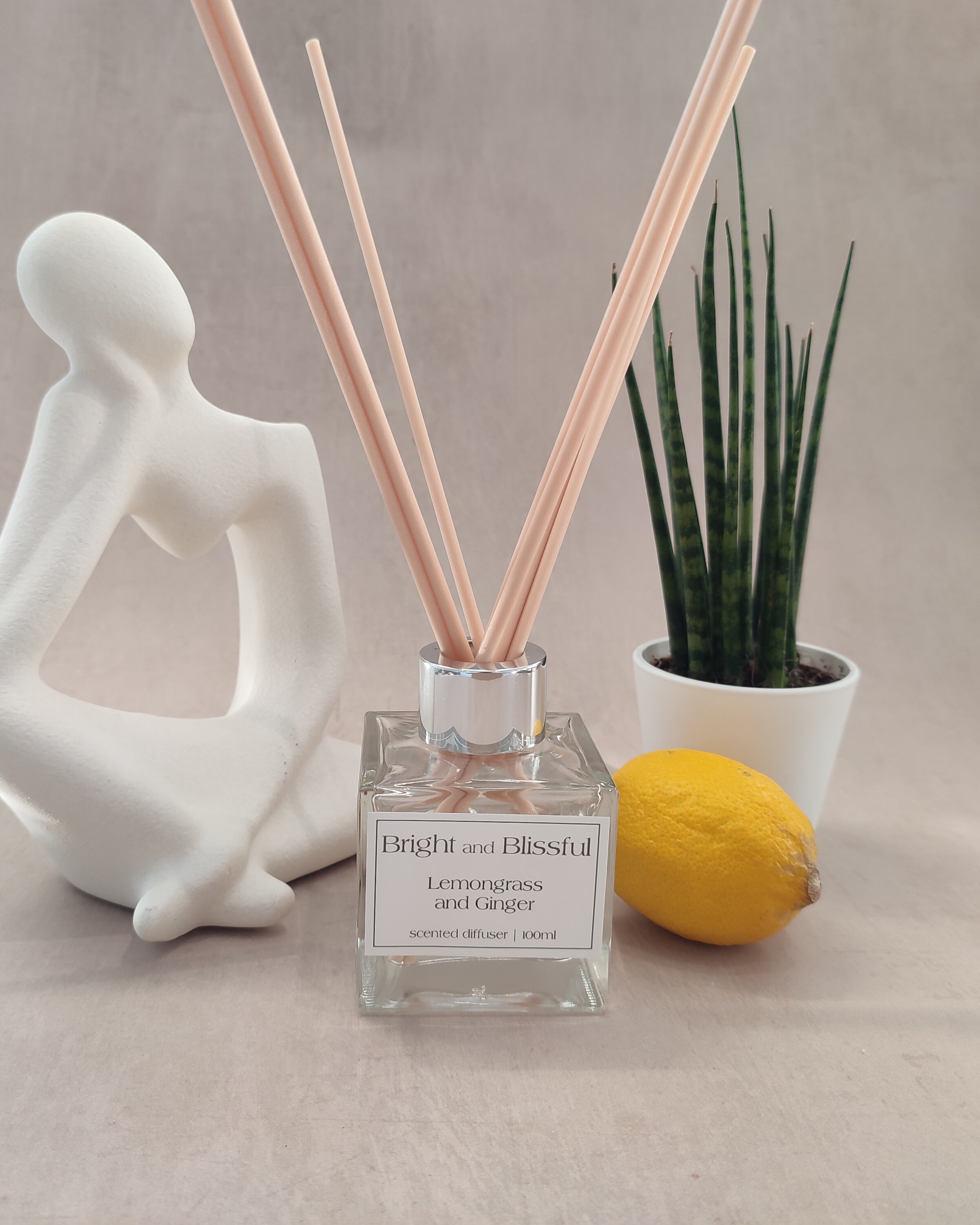 Reed diffuser with sticks, a lemon, and a decorative figure on a neutral background