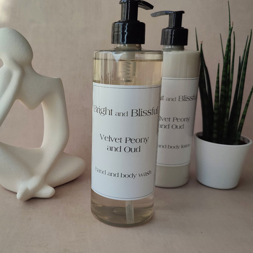 Two bottles of 'Bright and Blissful' hand and body wash on a neutral background with a plant and sculpture.