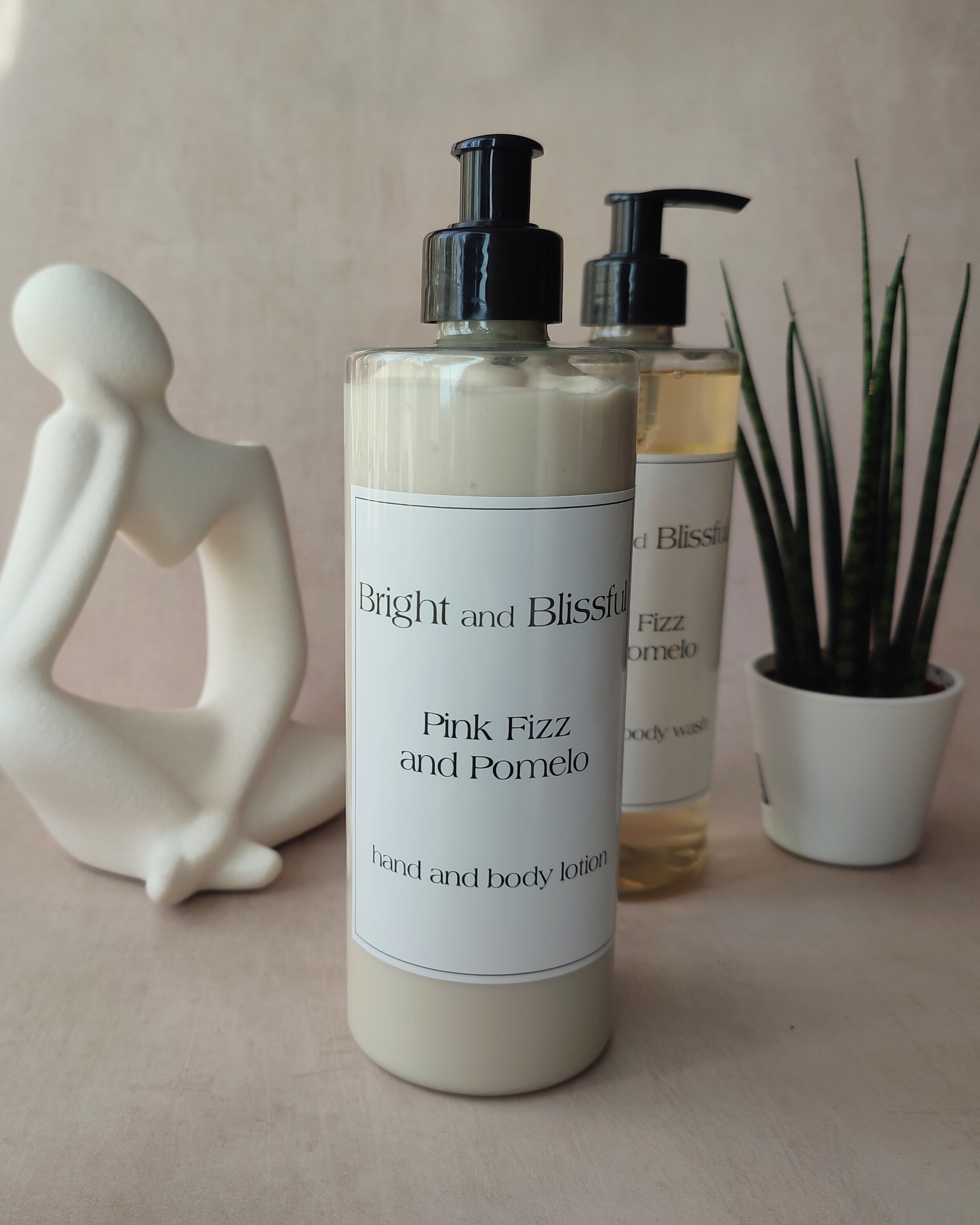 Hand and body lotion bottle with pump, decorative statue, and plant on a neutral background