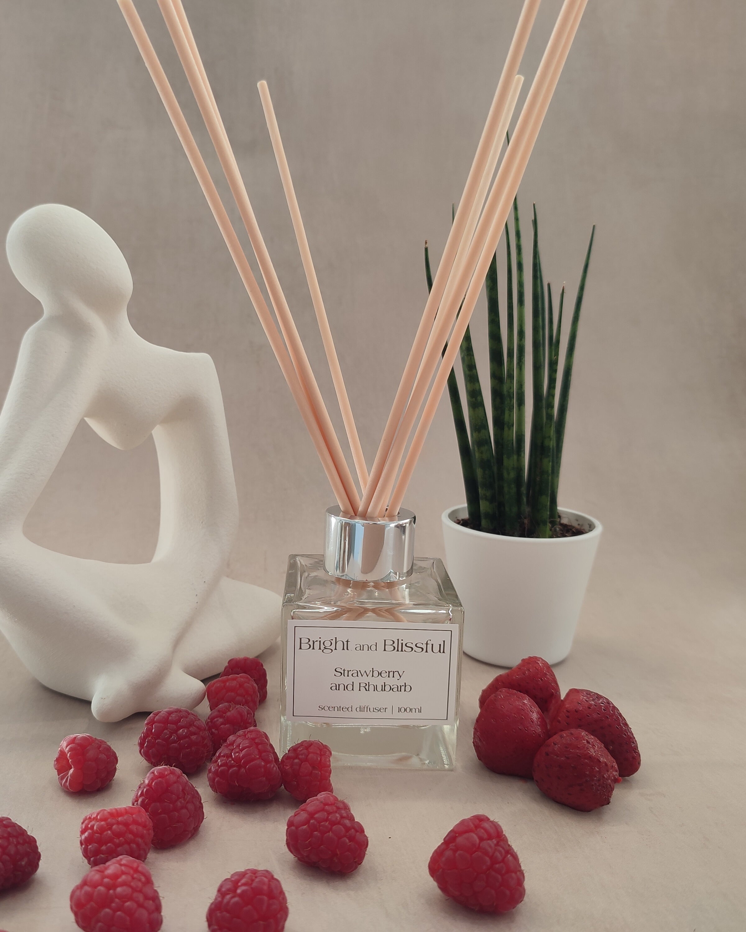 Reed diffuser with strawberries and a decorative figure on a neutral background