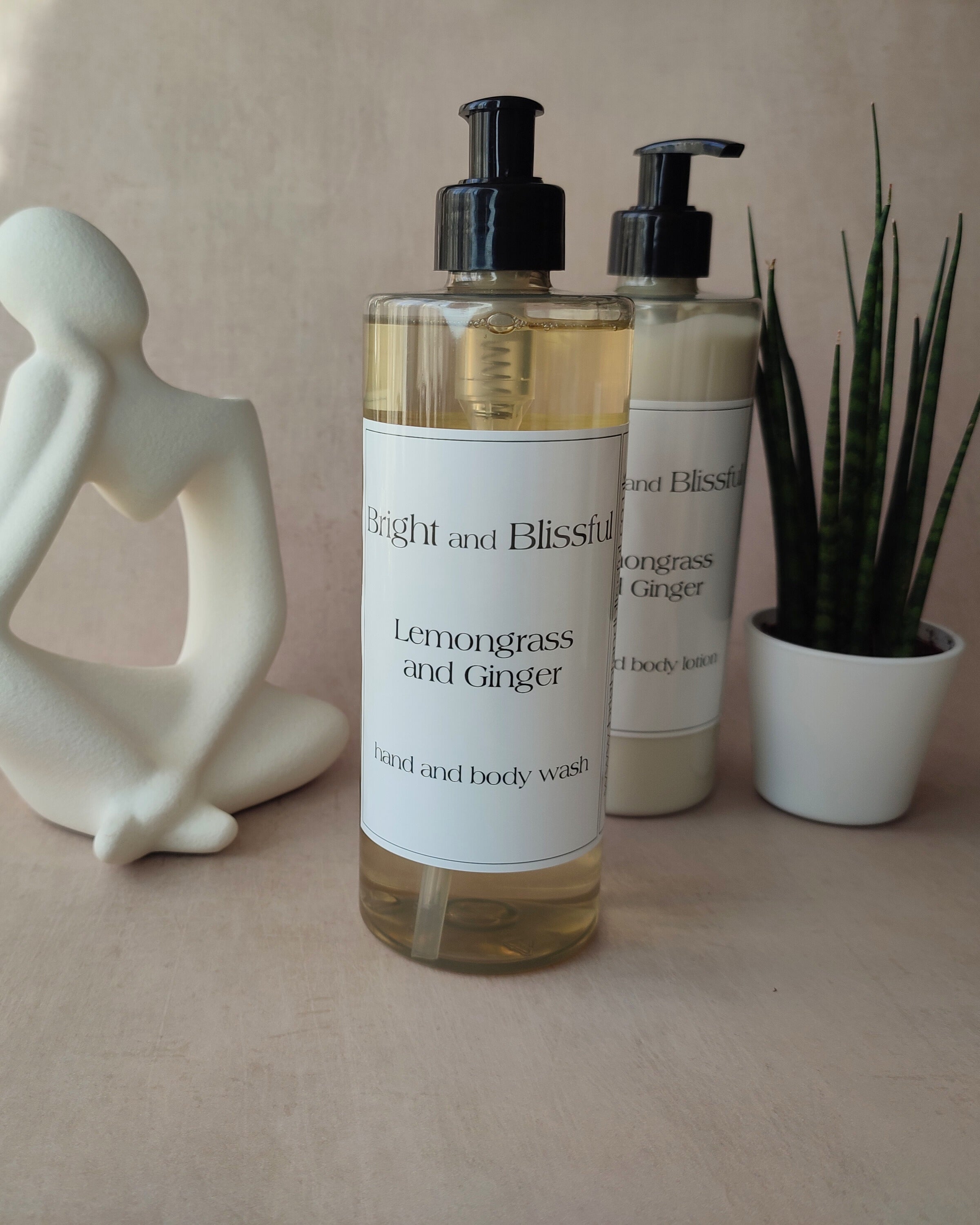 Bottle of 'Bright and Blissful' Lemongrass and Ginger hand and body wash on a neutral background with a decorative figure and plant.