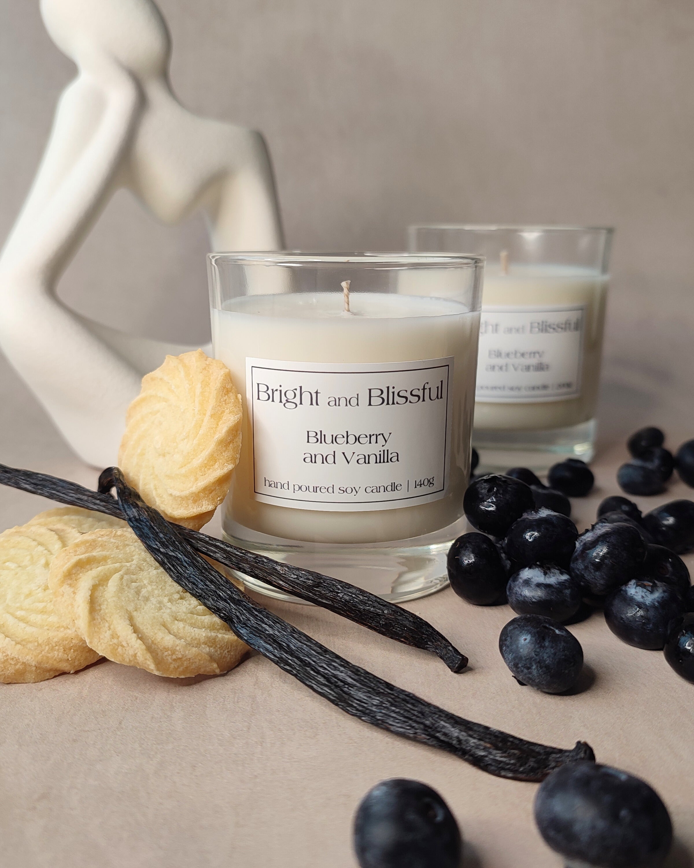 Candle labeled 'Bright and Blissful' with blueberries, vanilla beans, and cookies on a neutral background
