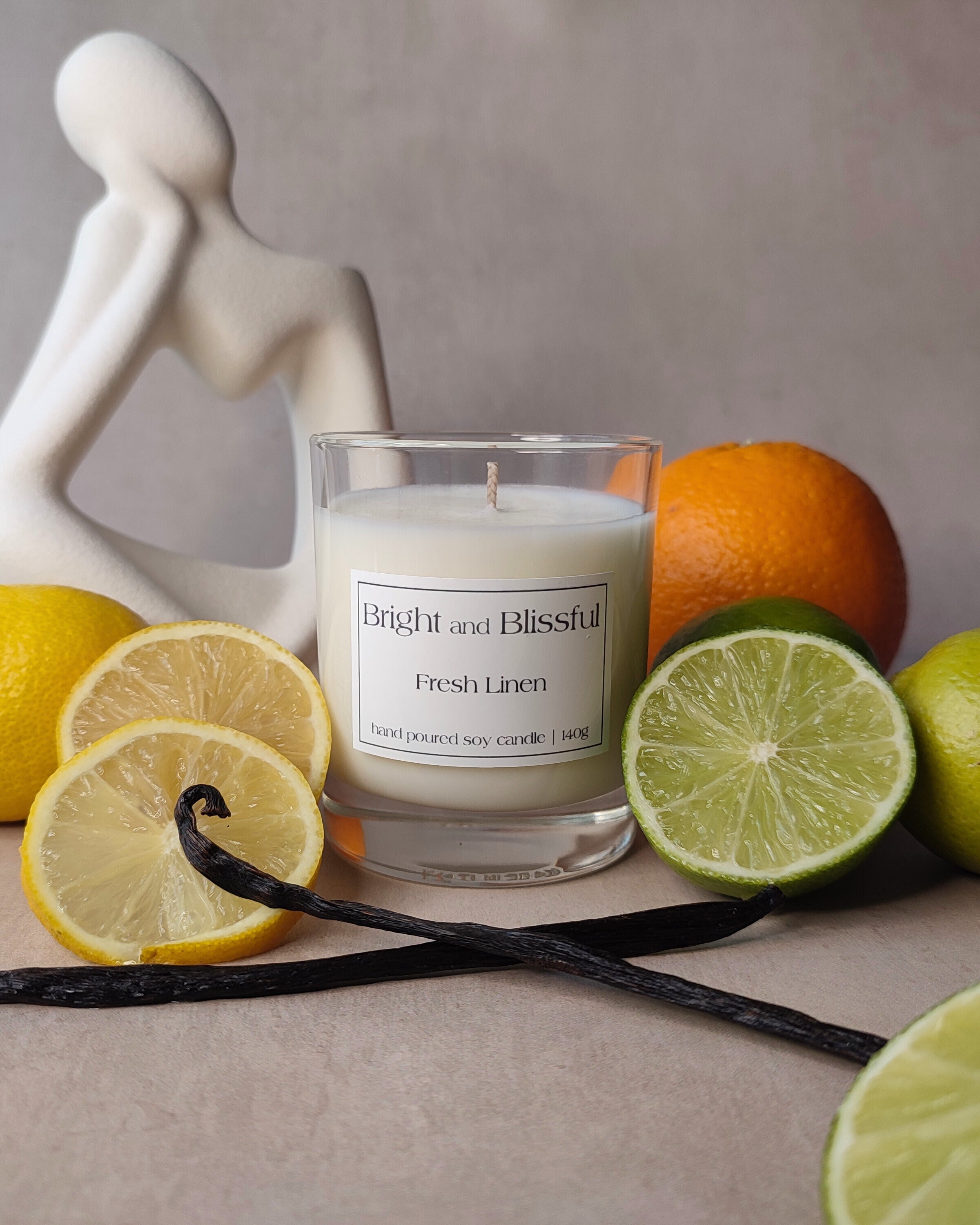 Candle labeled 'Bright and Blissful' surrounded by lemons, limes, and oranges on a neutral background