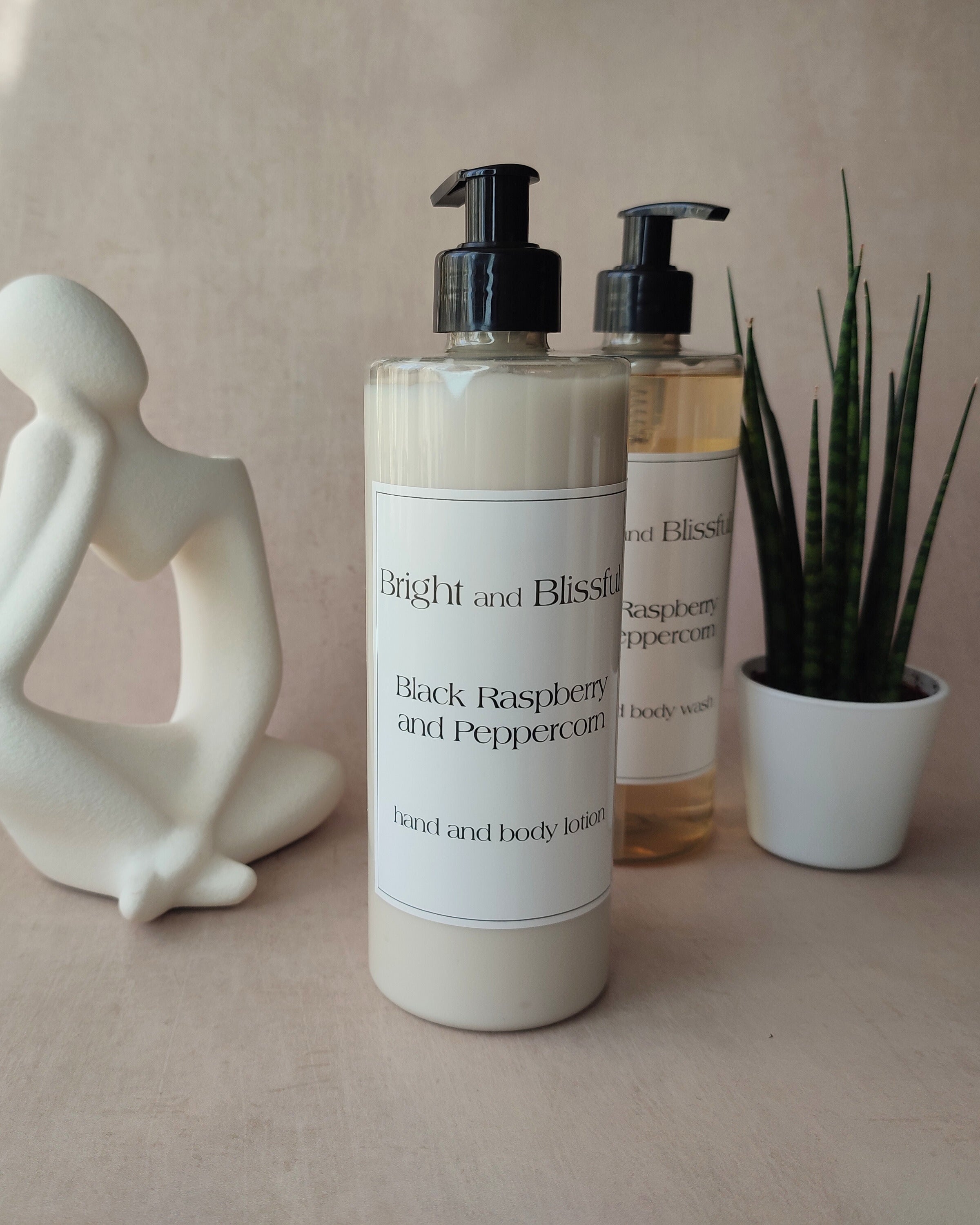 Two bottles of 'Bright and Blissful' body wash on a neutral surface with a decorative figure and plant.
