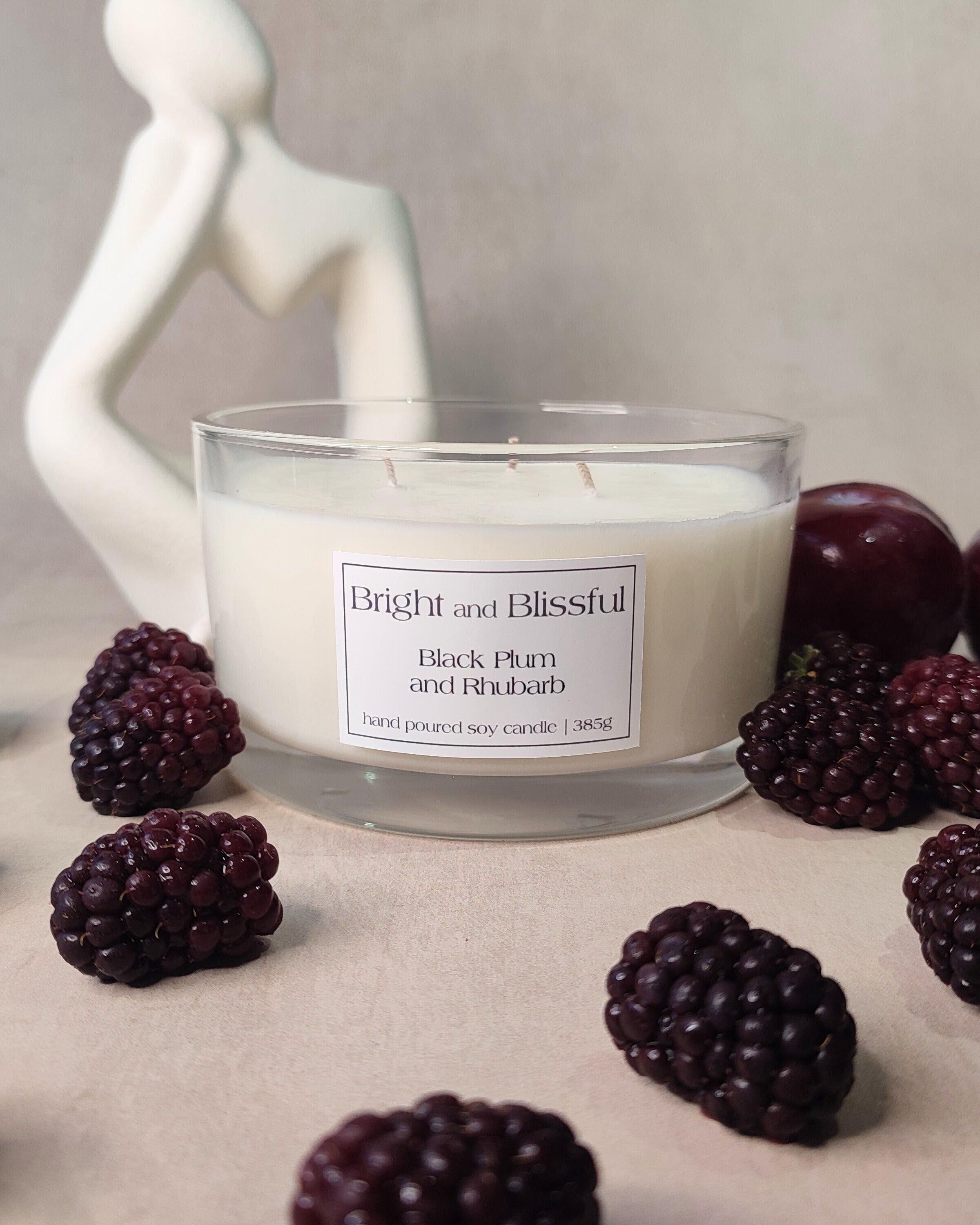candle surrounded with a white statue,blackcurrants and a plum