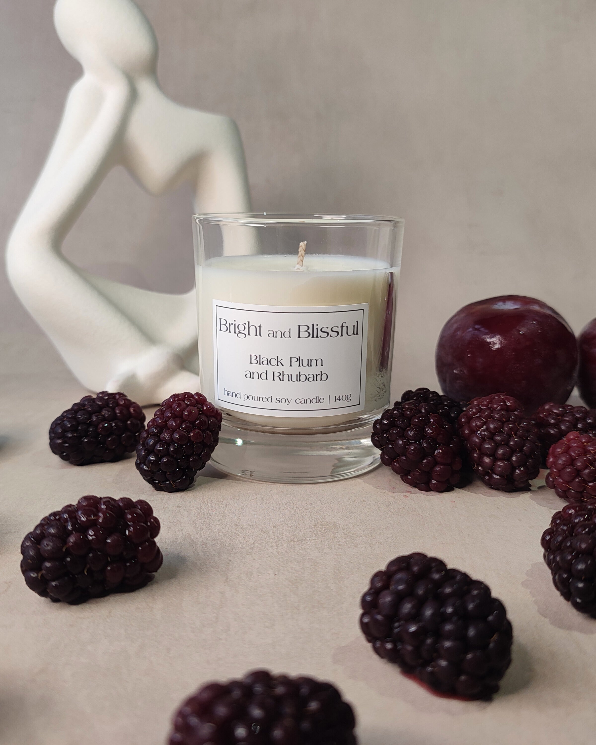 candle surrounded with a white statue,blackcurrants and a plum