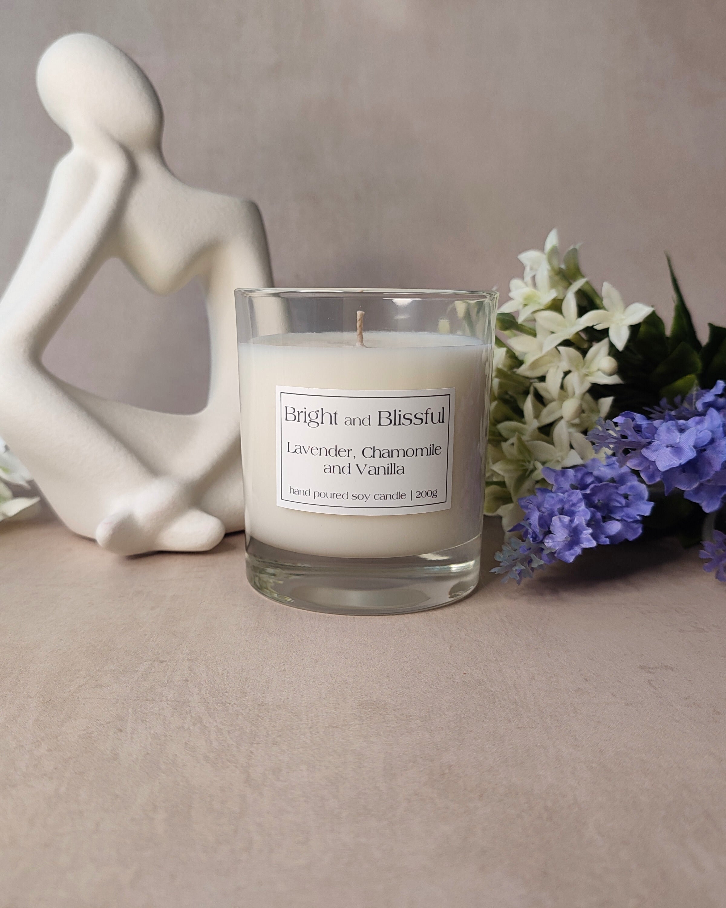 Candle labeled 'Bright and Blissful' with a decorative figure and flowers on a neutral background