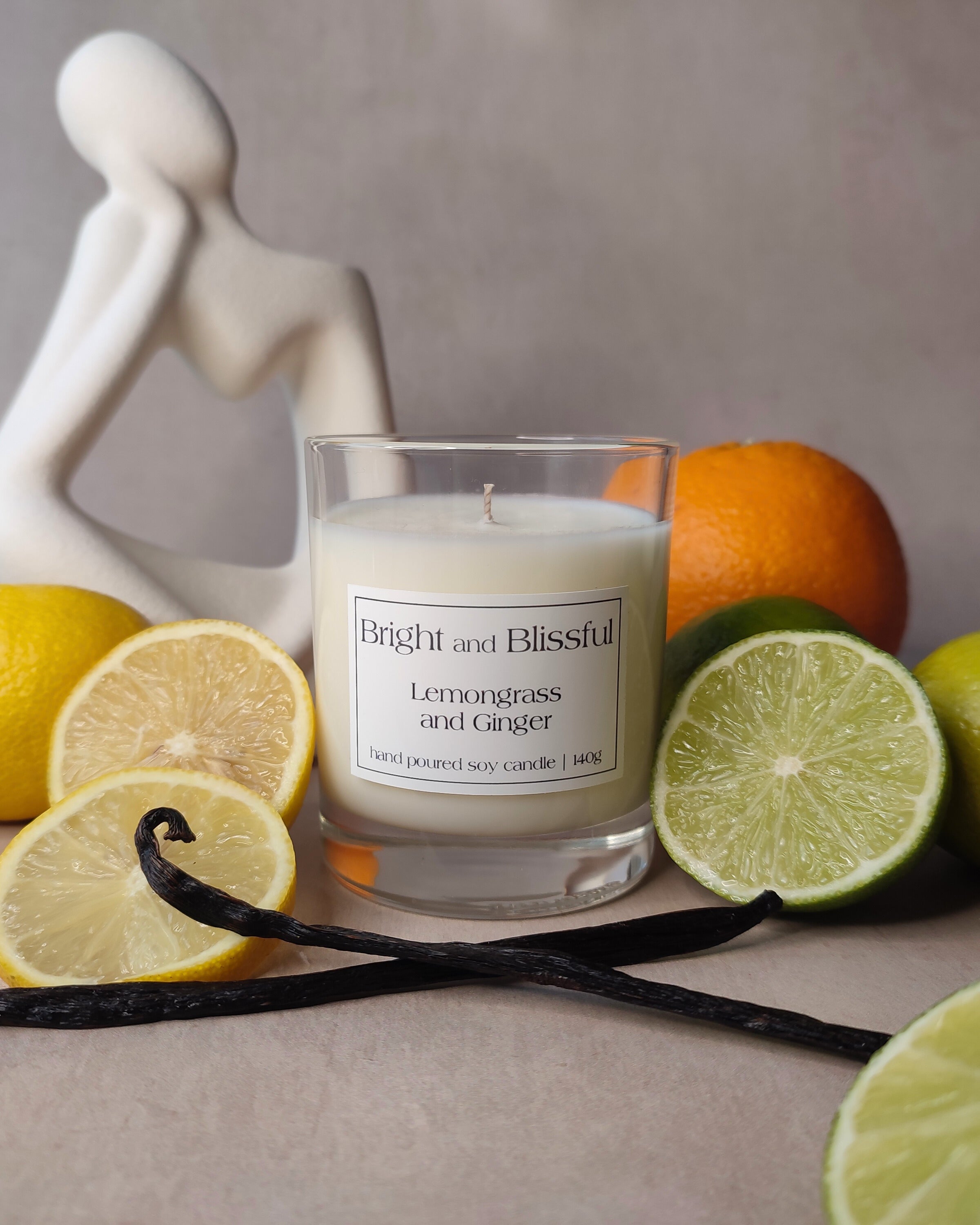 Candle labeled 'Bright and Blissful' surrounded by lemons, limes, and oranges on a neutral background