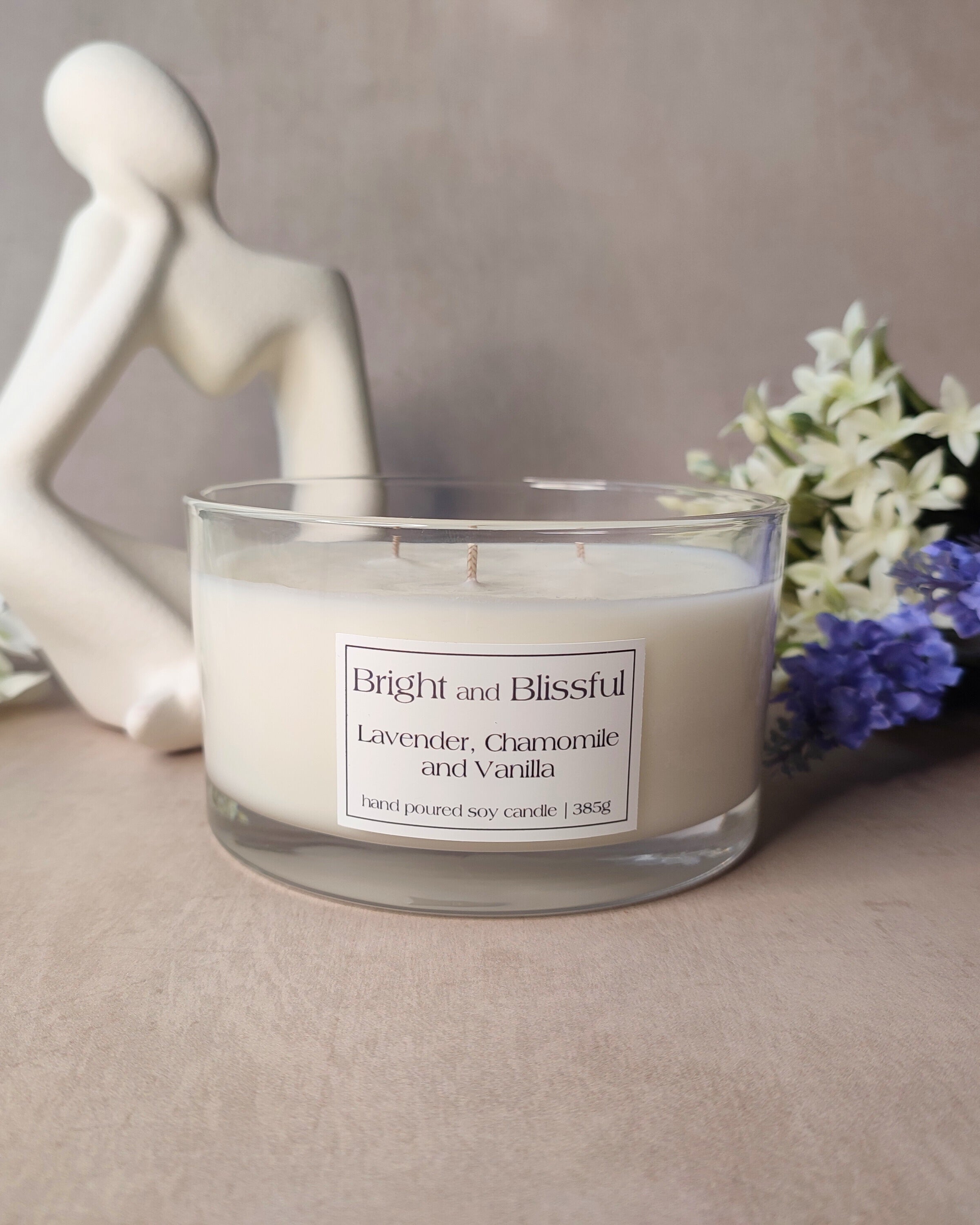 Candle labeled 'Bright and Blissful' with a decorative figure and flowers in the background