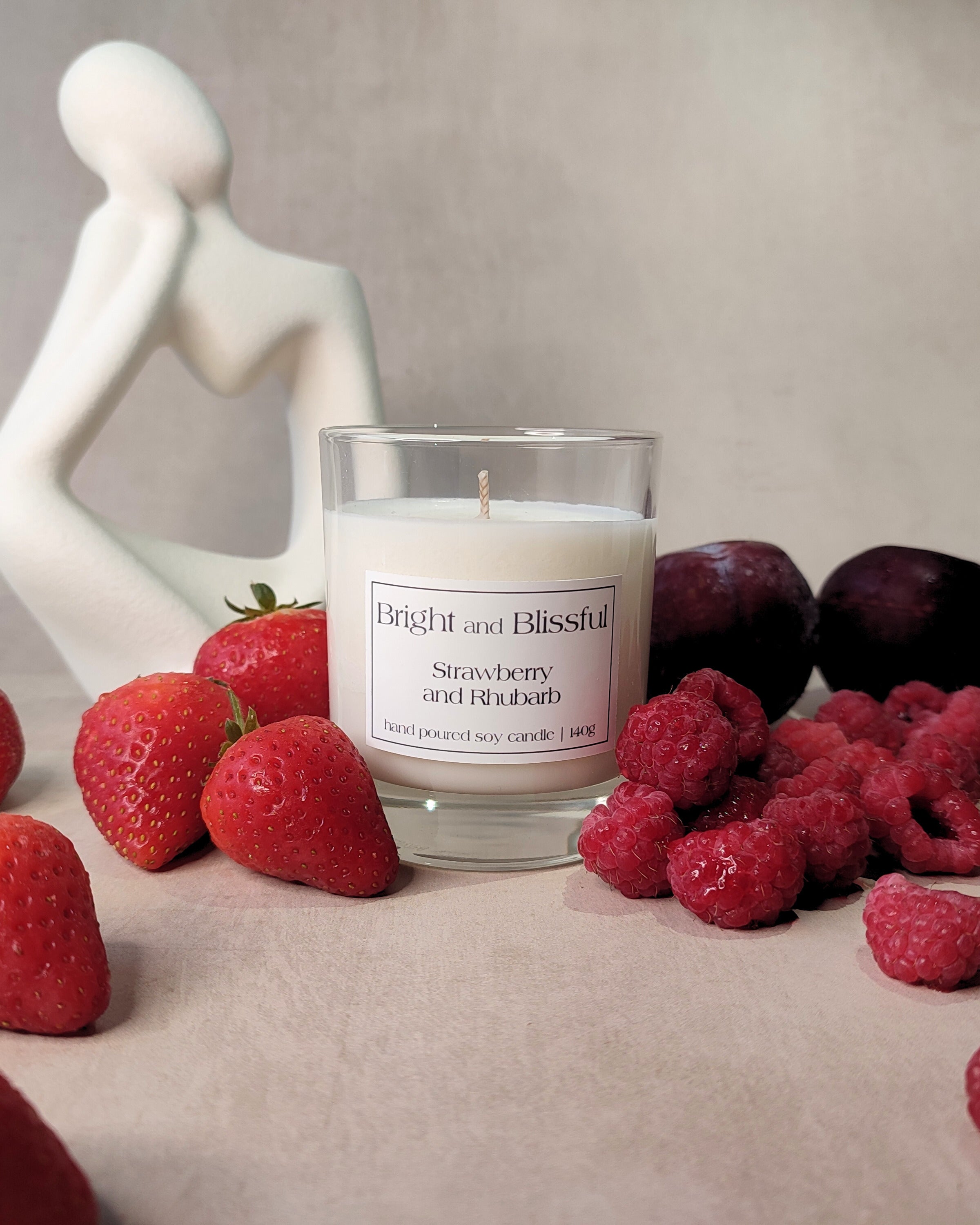 Candle labeled 'Bright and Blissful' surrounded by strawberries and raspberries on a neutral background