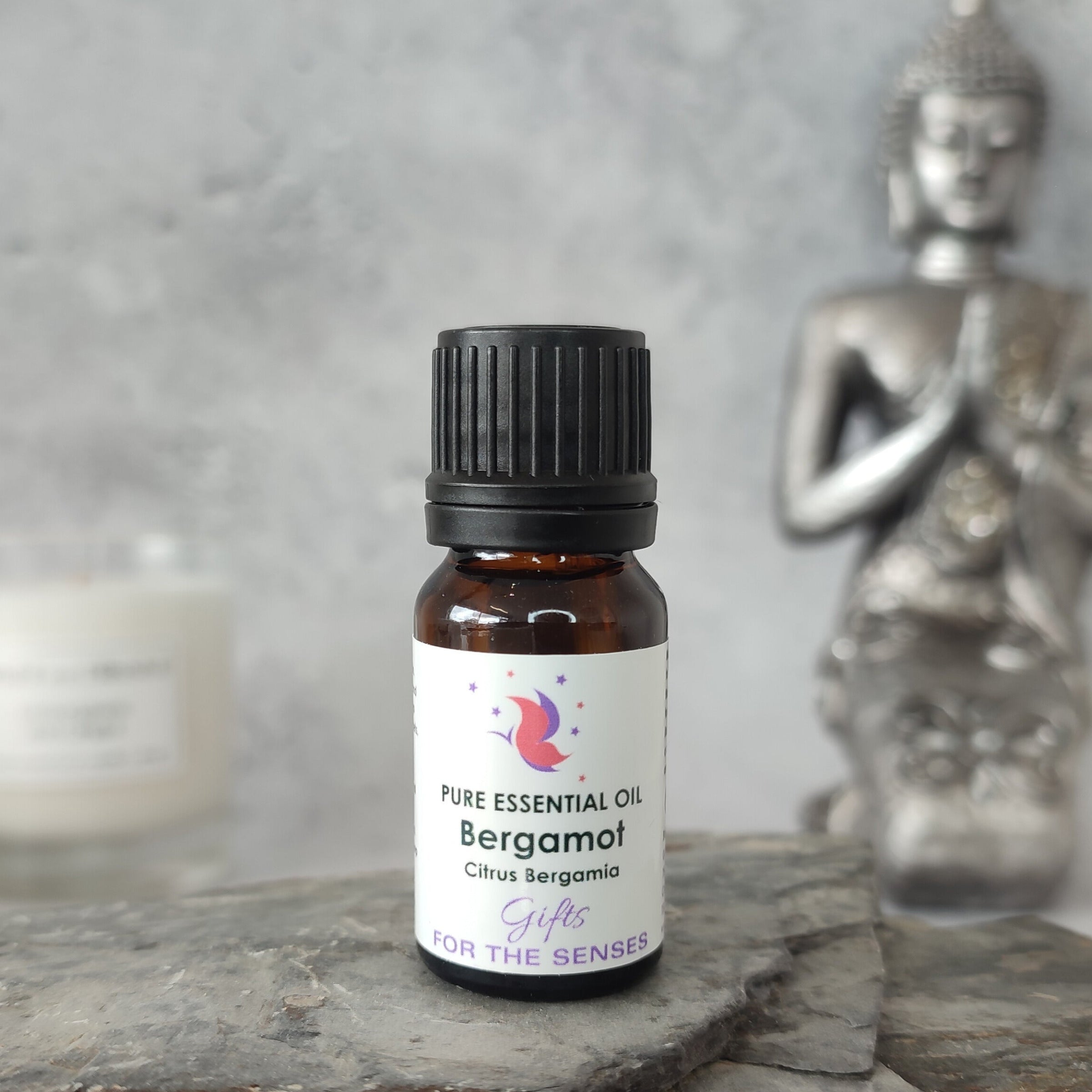 Bottle of Bergamot essential oil on a slate surface with a Buddha statue in the background