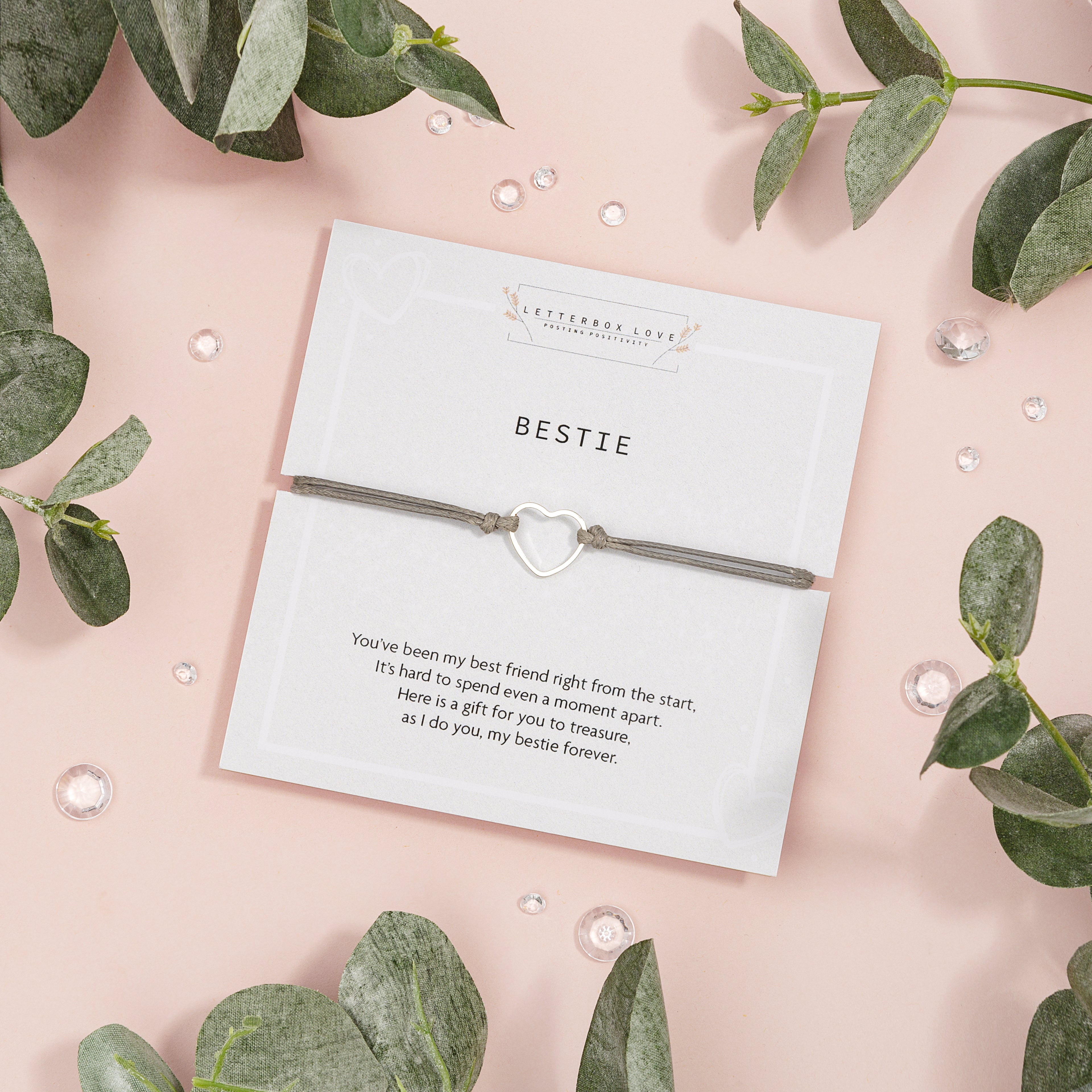 Card with a heart-shaped grey cord bracelet and decorative text on a pink background with green leaves.