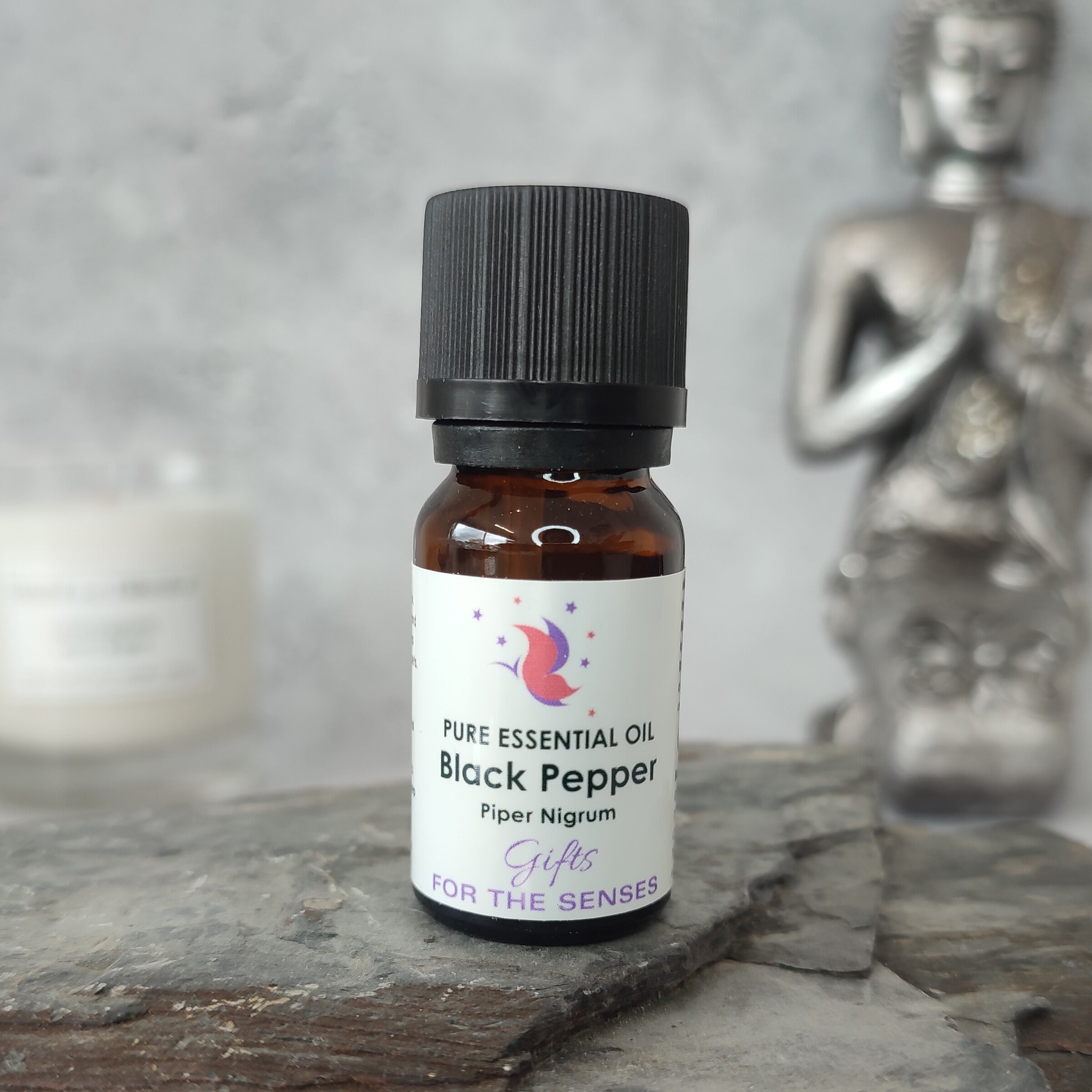 Bottle of pure essential oil labeled 'Black Pepper' on a stone surface with a Buddha statue in the background.