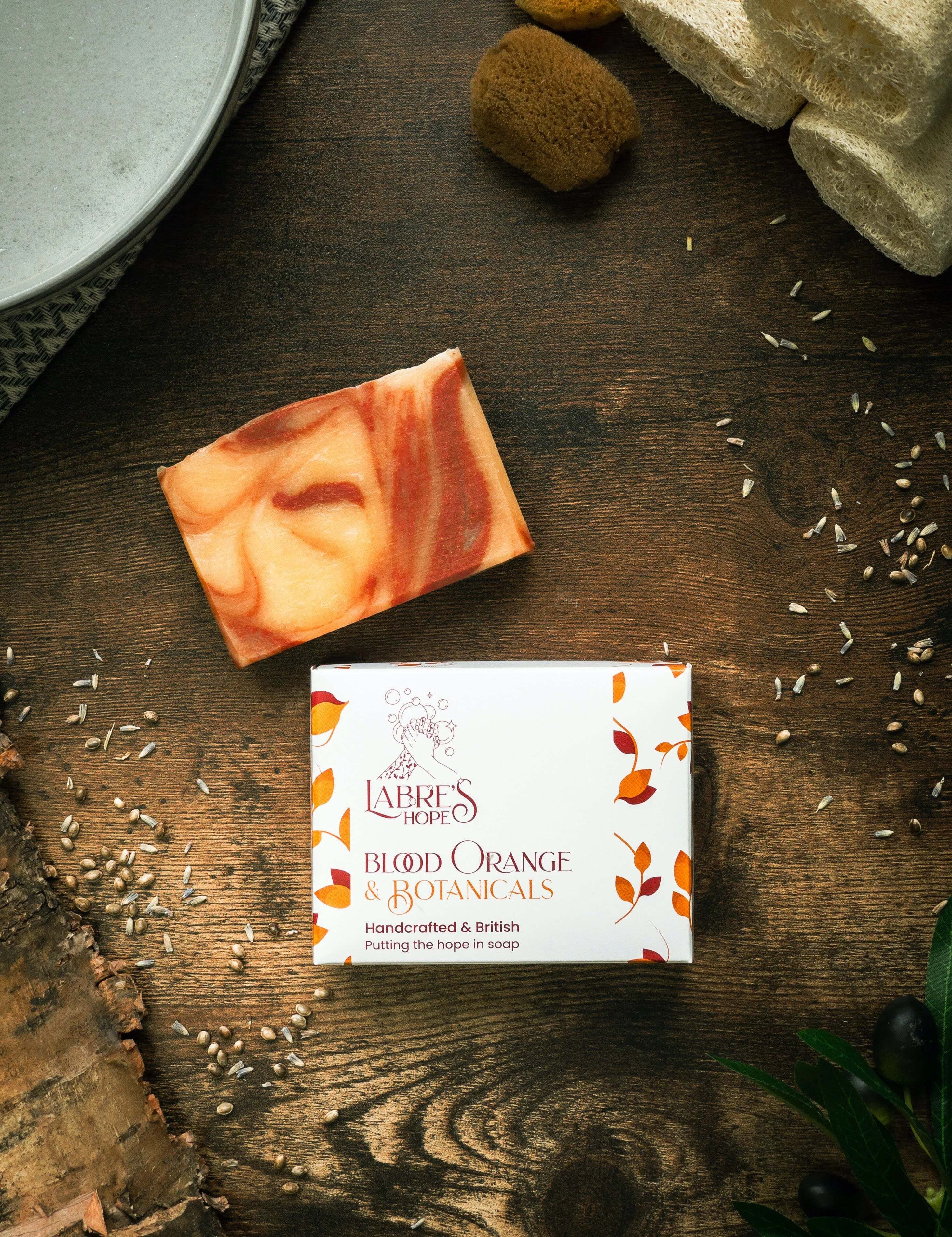 Marbled soap bar and box labelled 'Labre's Blood Orange Botanicals' on a wooden surface.