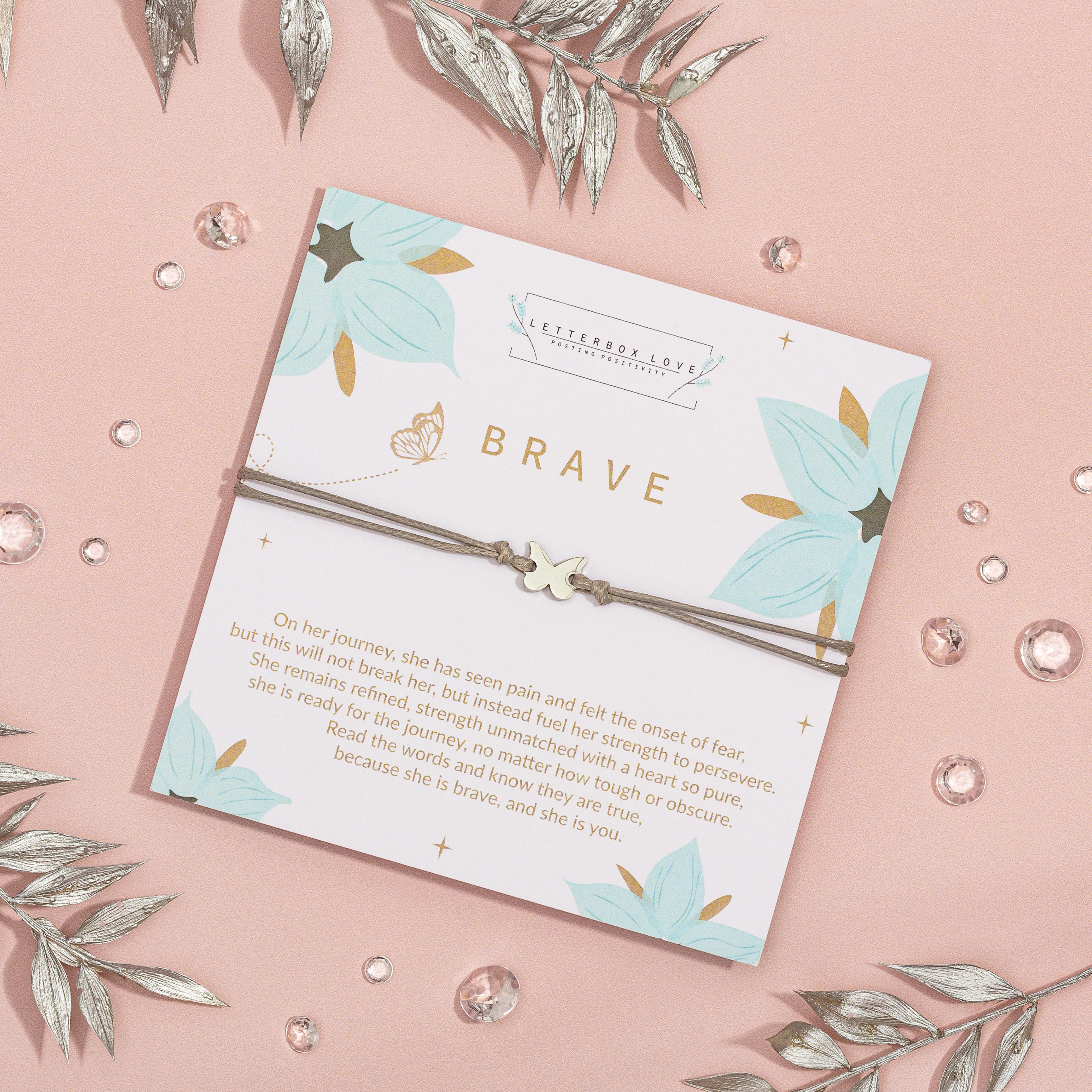 Bracelet with 'BRAVE' card on a pink background with decorative elements
