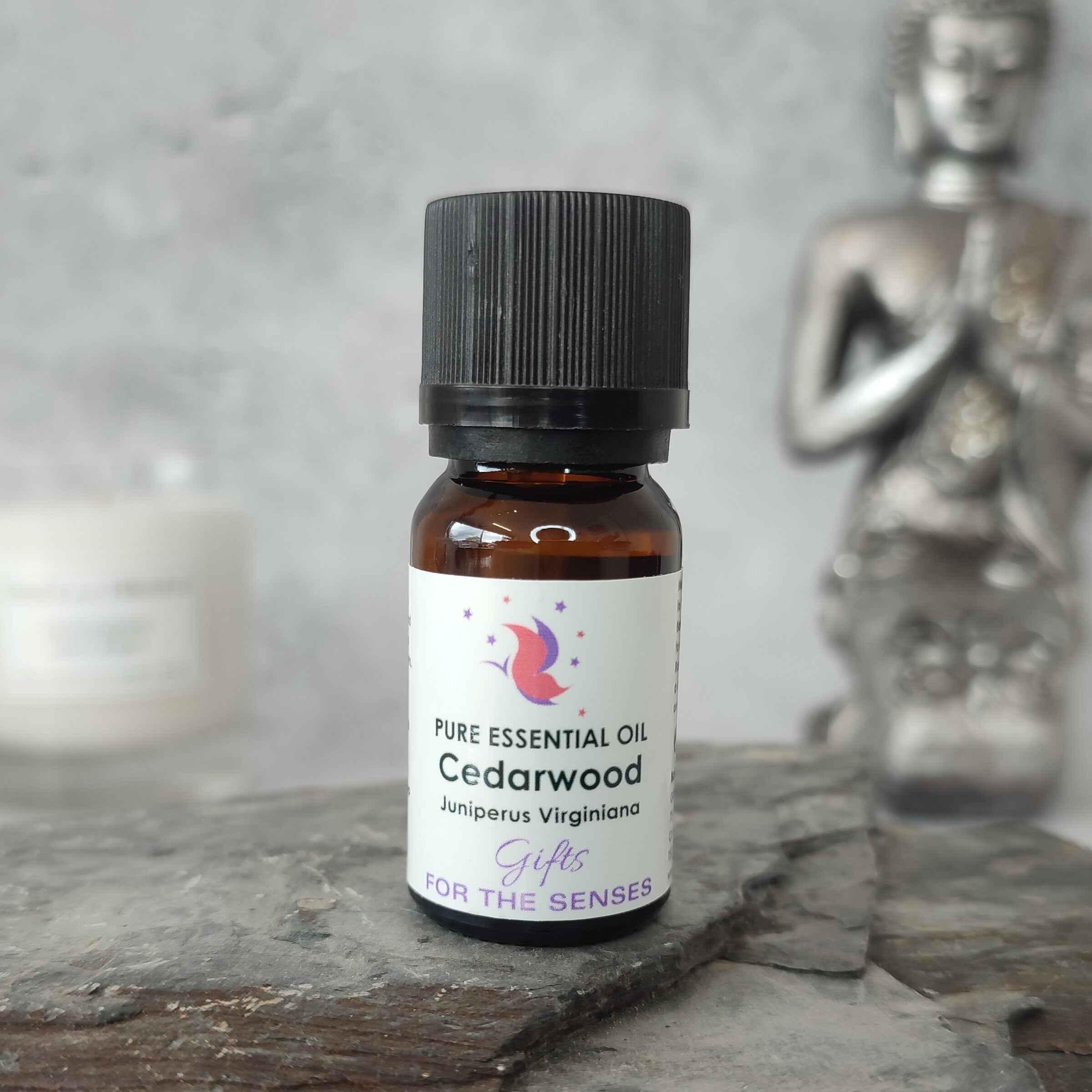 Bottle of Cedarwood essential oil on a wooden surface with a Buddha statue in the background.