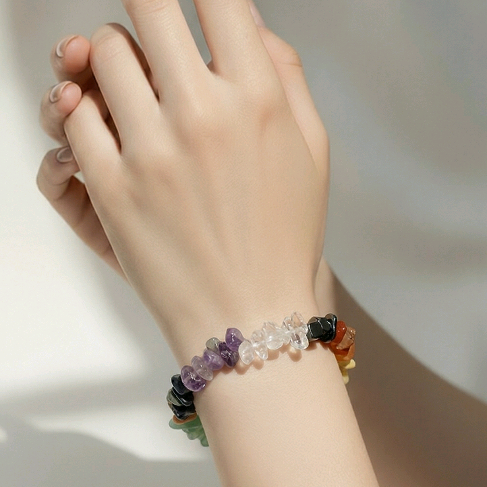 Hand wearing a chakra chip bracelet on a neutral background