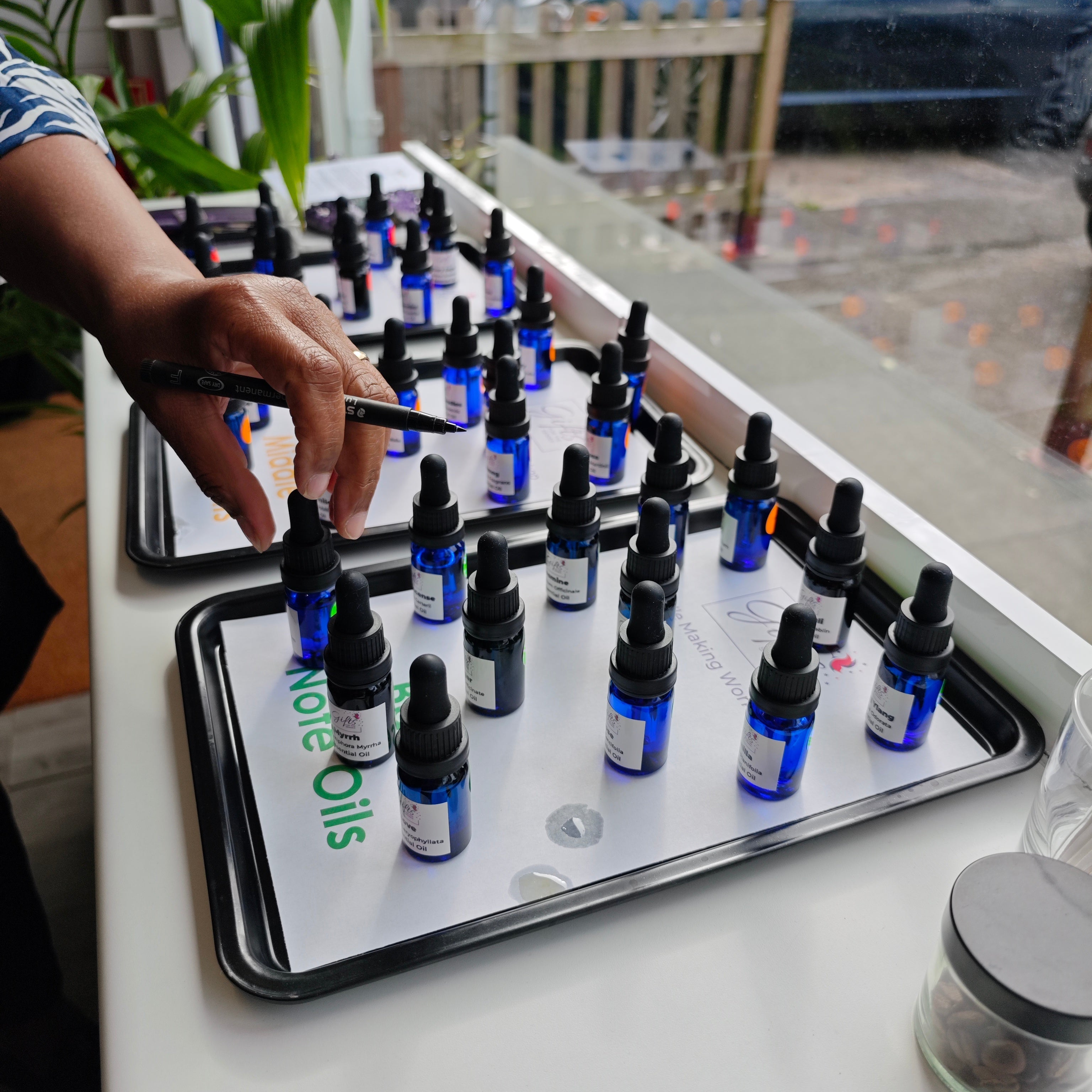 Bottles of 'essential oils on trays next to a window with a person's hand reaching towards one of them.