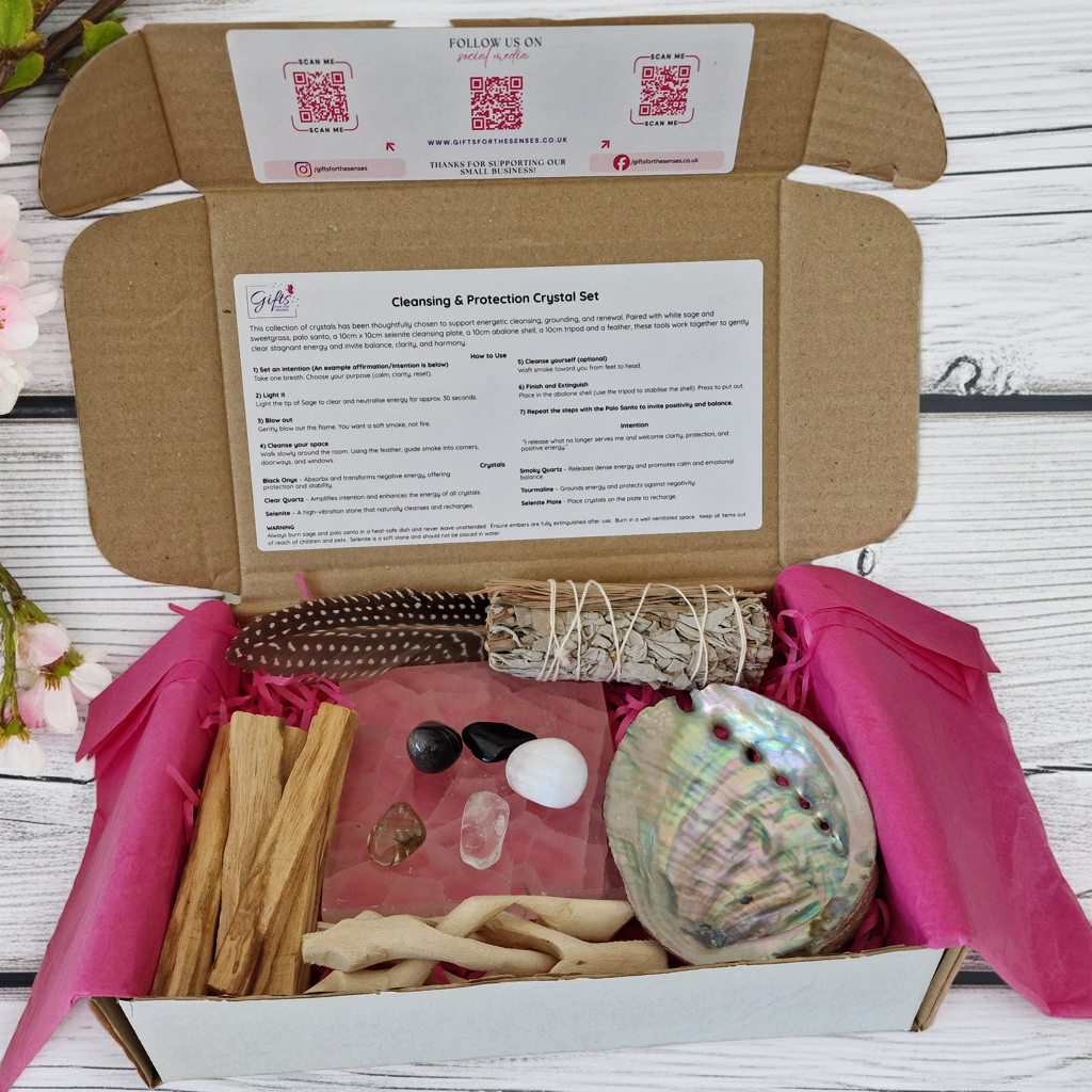 Crystal set with a shell, candles, and other items in an open cardboard box on a wooden surface.