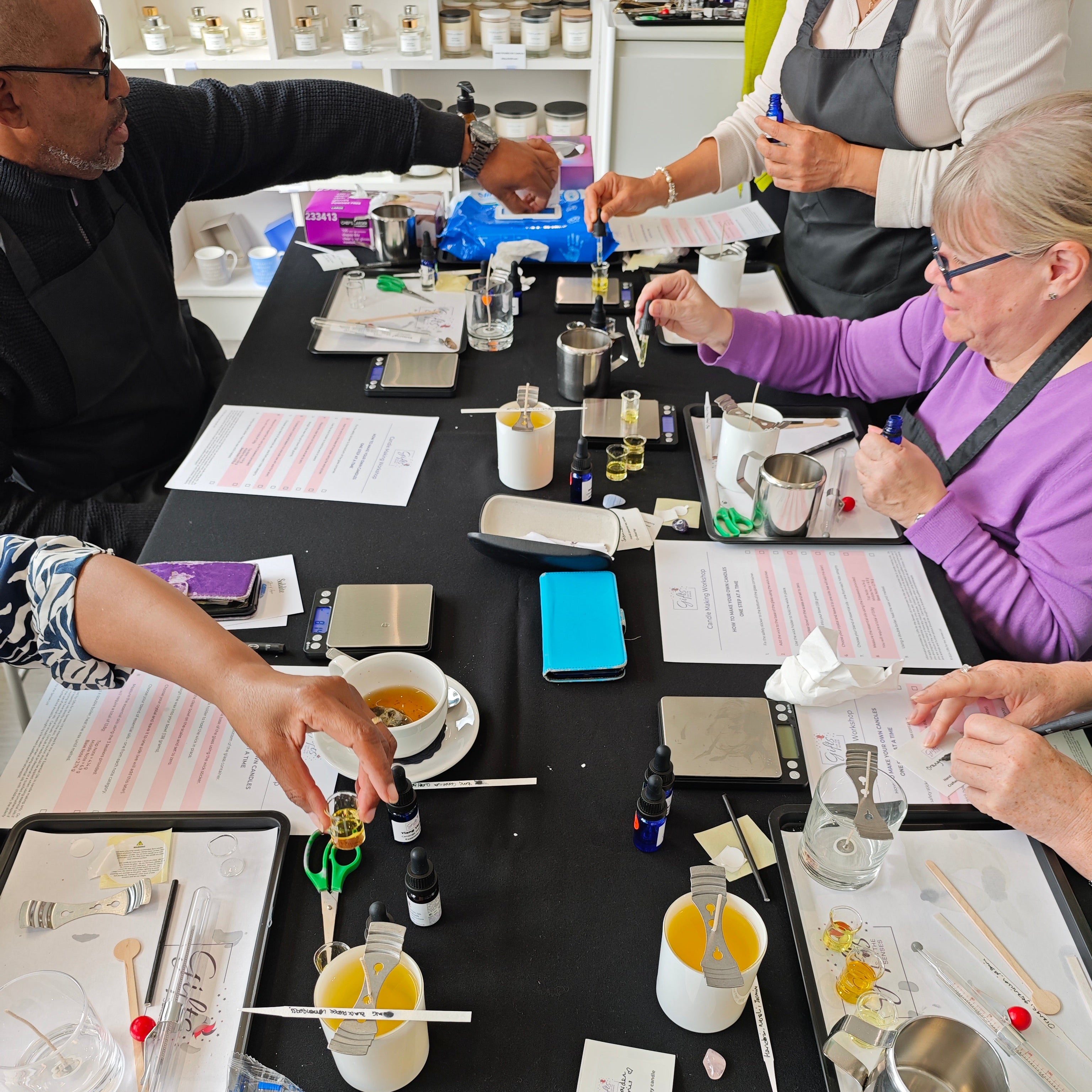 Group of people engaged in a candle making workshop at a table with various materials and tools.