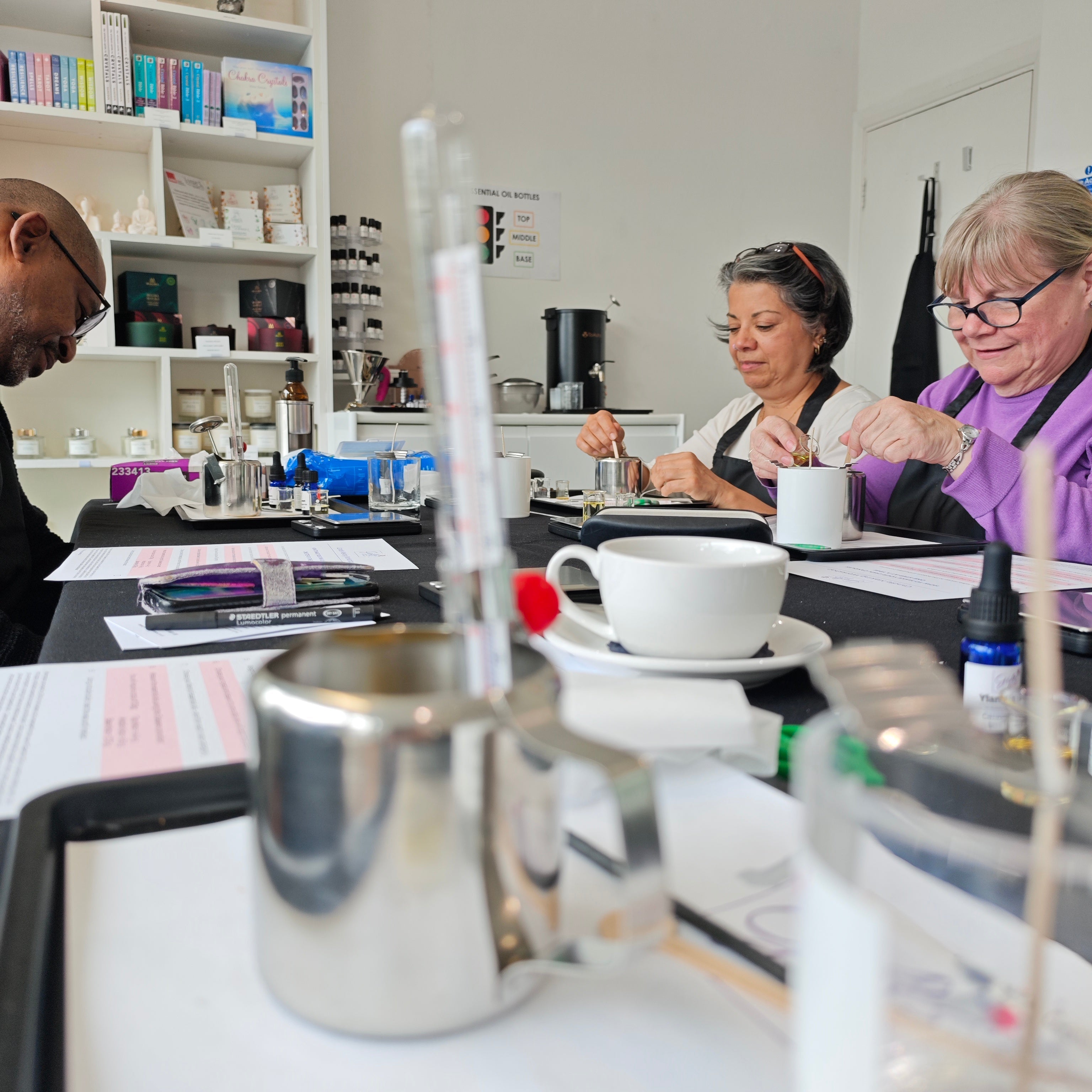 Three people sitting at a table with coffee cups and books in a room.