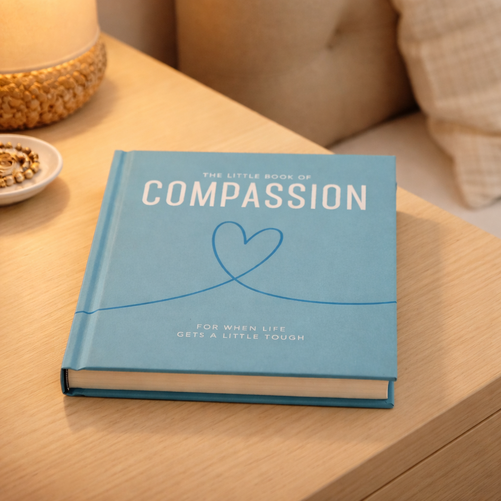 Blue book titled 'The Little Book of Compassion' on a wooden surface.