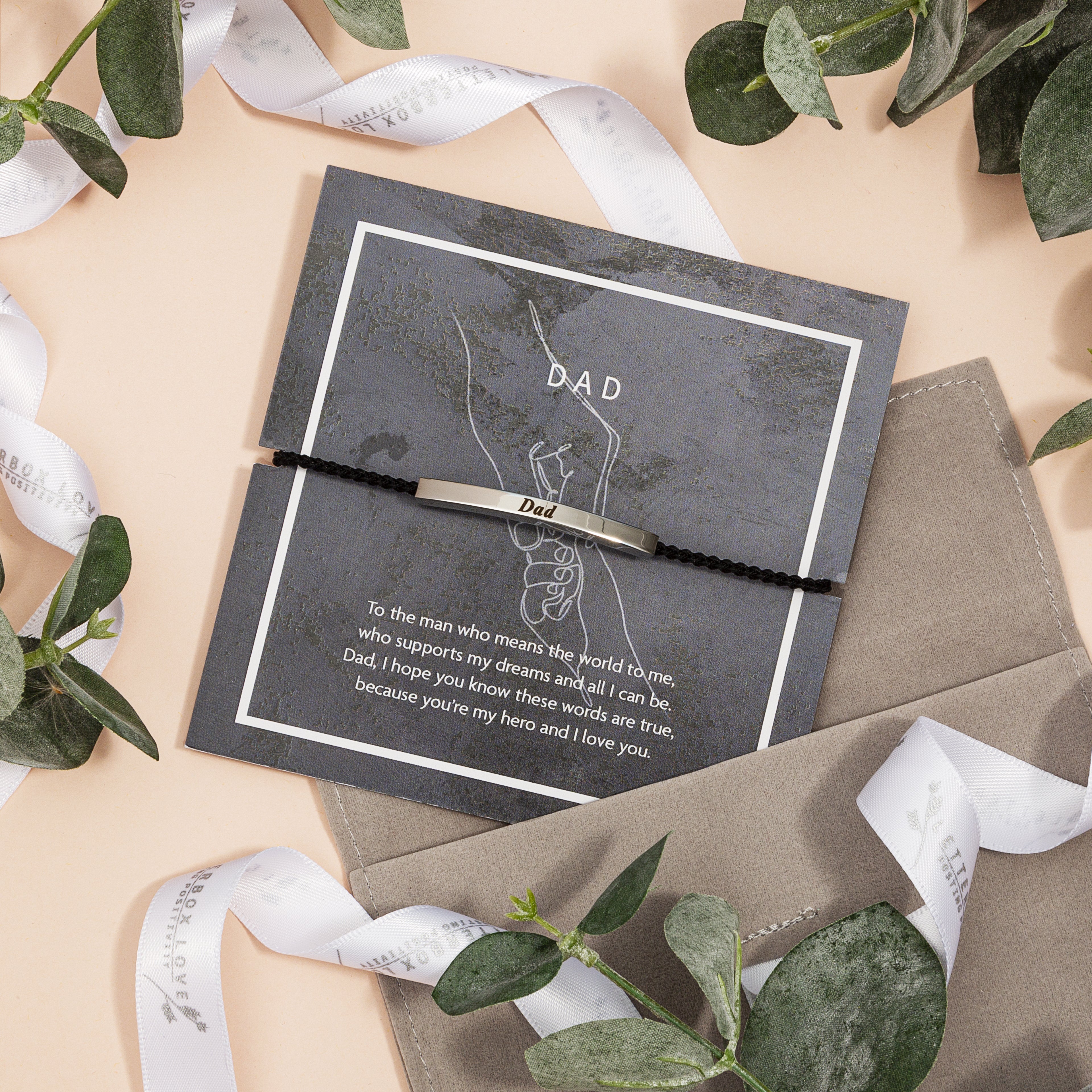 Personalized bracelet and card set for a father on a decorative background with ribbons and leaves.