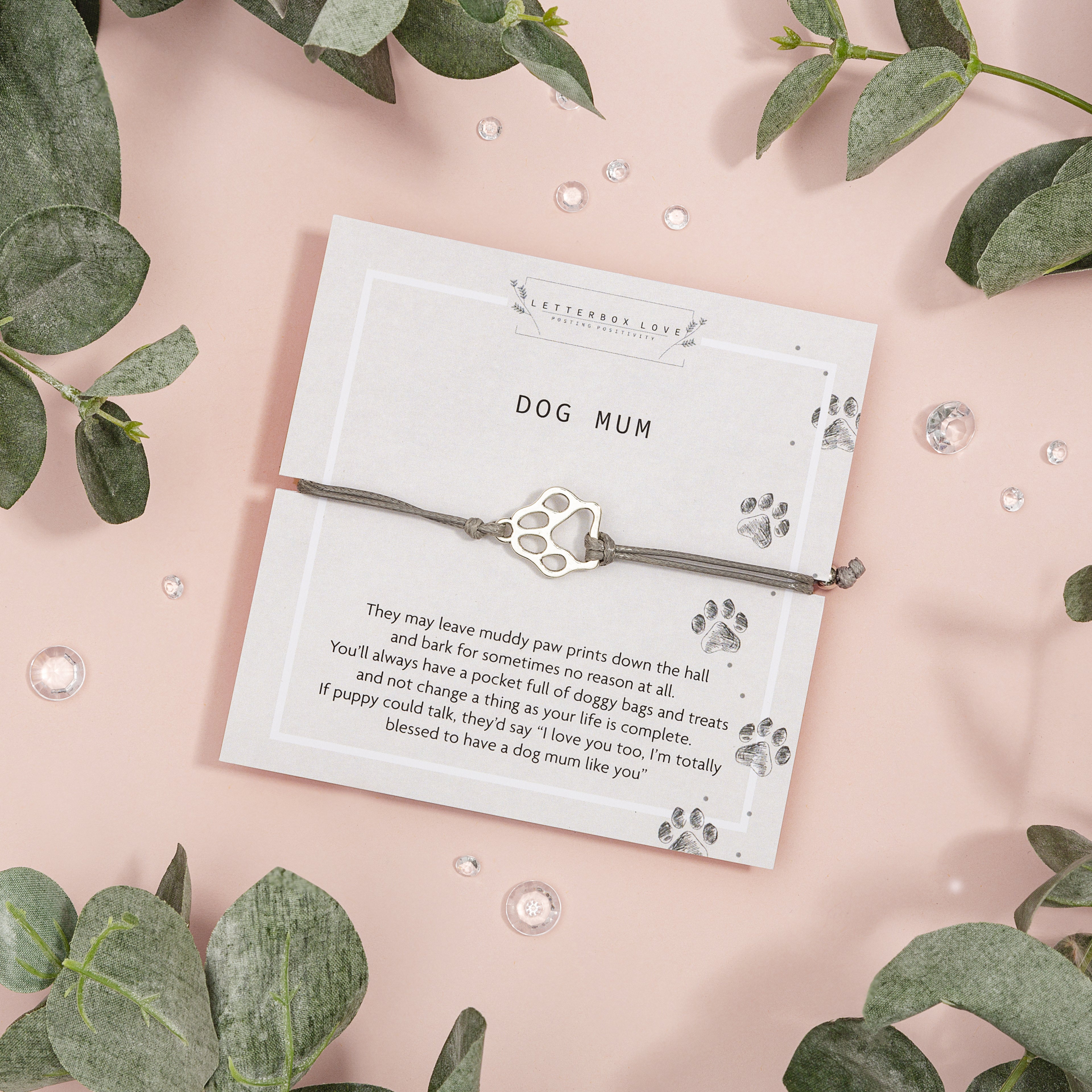 Bracelet on a card with text and paw print design, surrounded by green leaves on a pink background