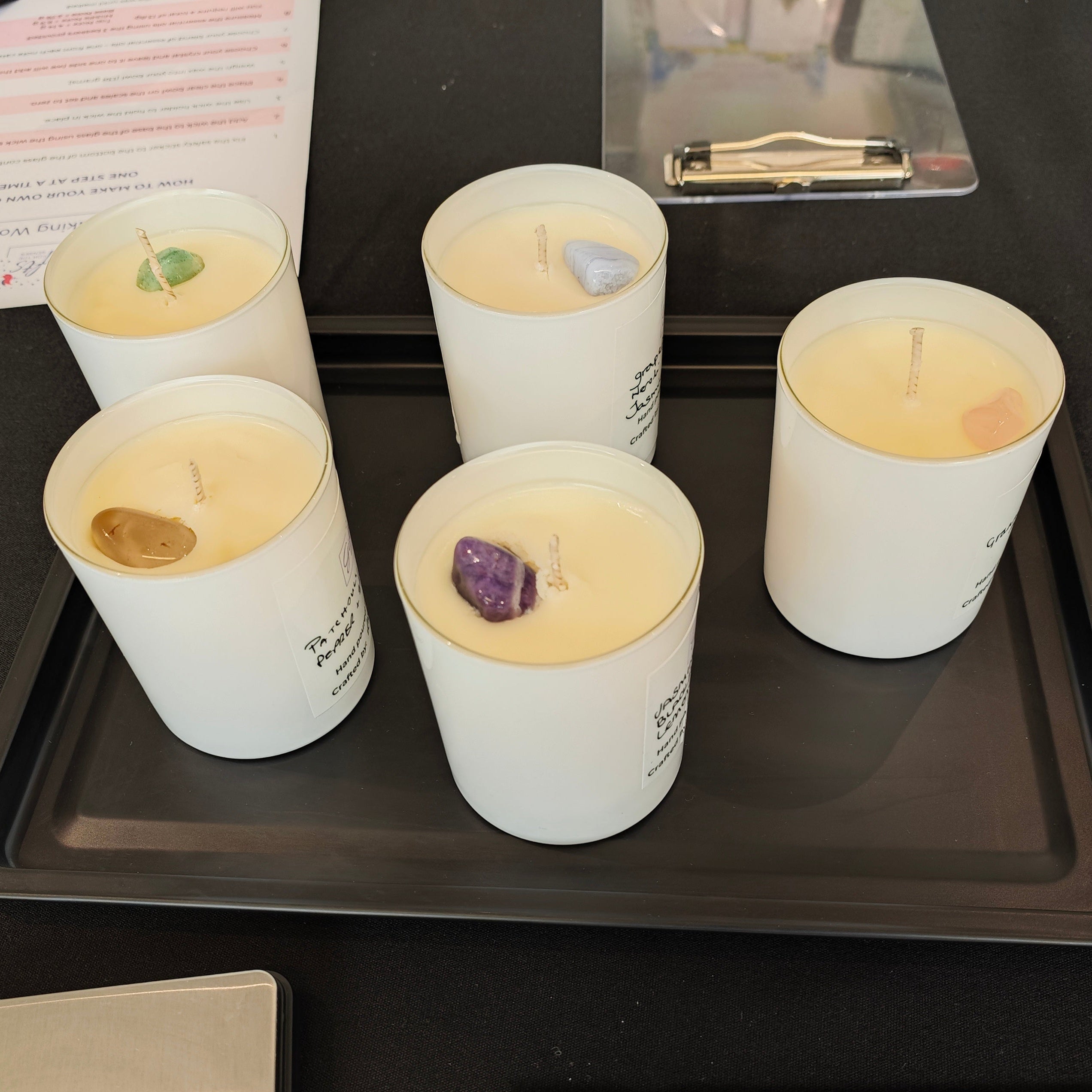 Candles in white containers on a black tray with other items on a table