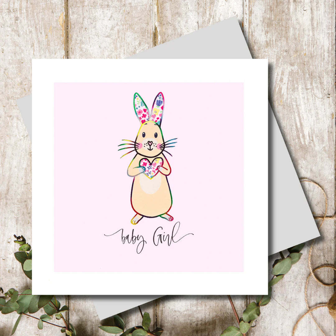 Greeting card with a rabbit illustration and 'baby girl' text on a wooden surface.