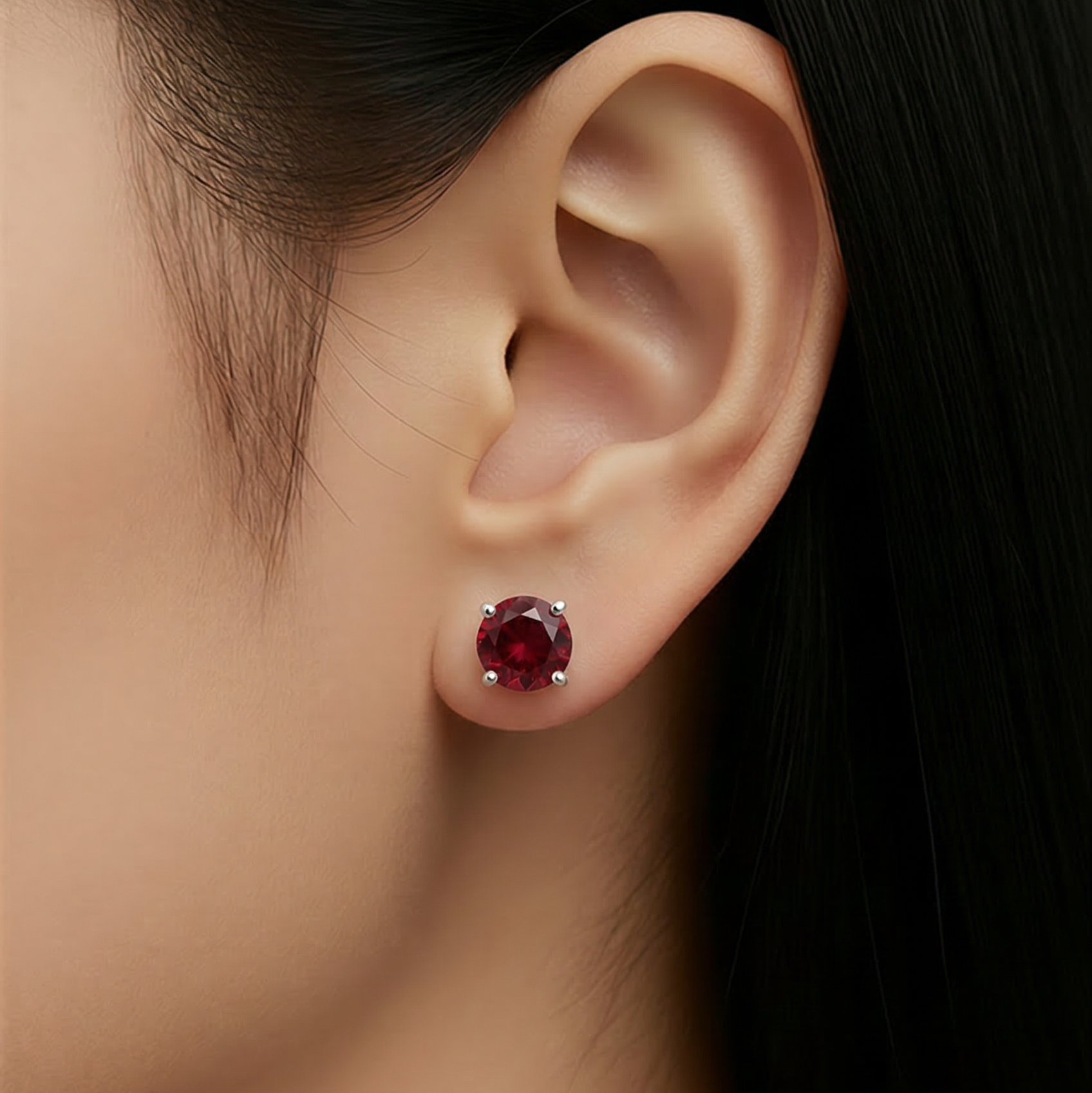 Close-up of an ear wearing a garnet gemstone earring with dark hair and skin background