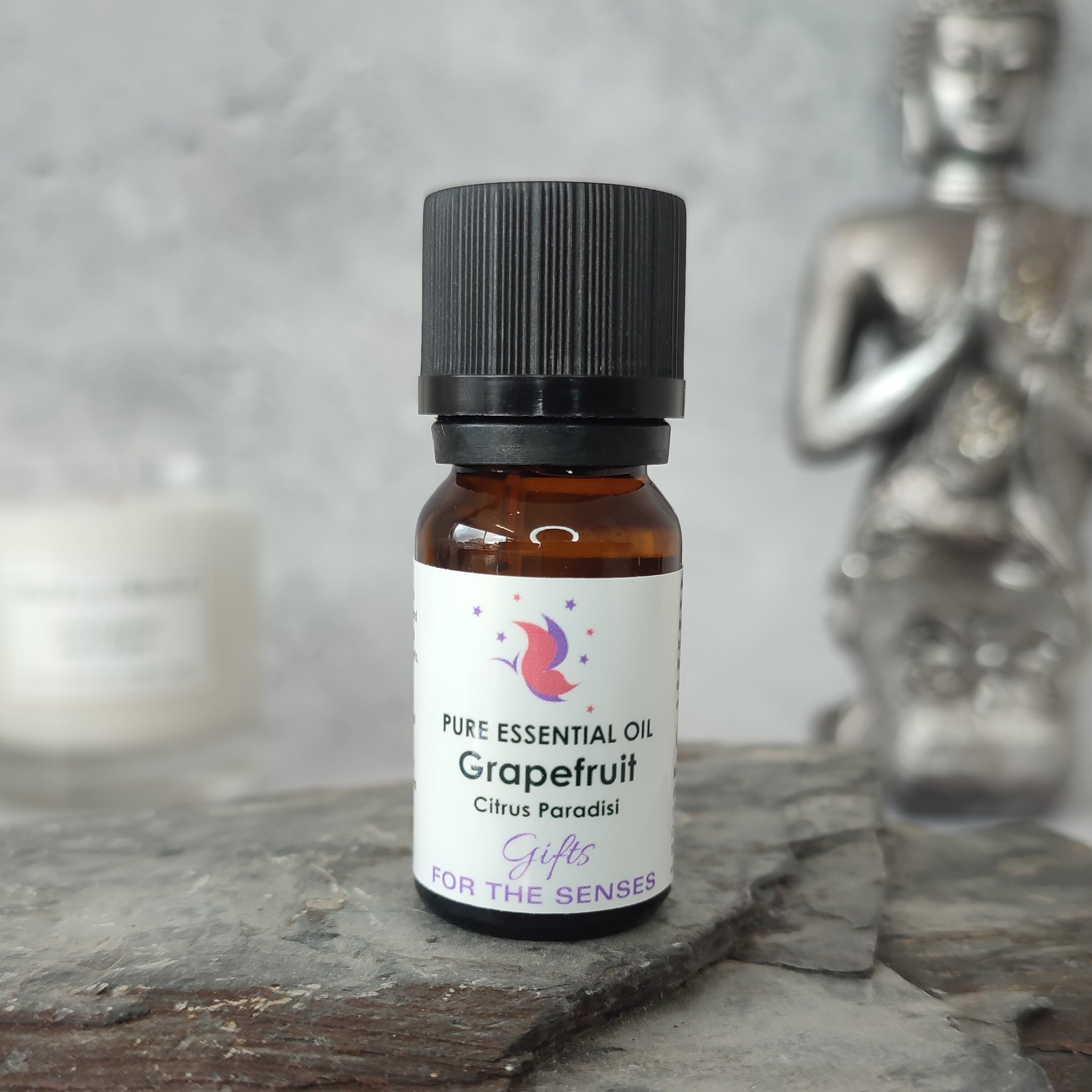 Bottle of grapefruit essential oil on a stone surface with a Buddha statue in the background