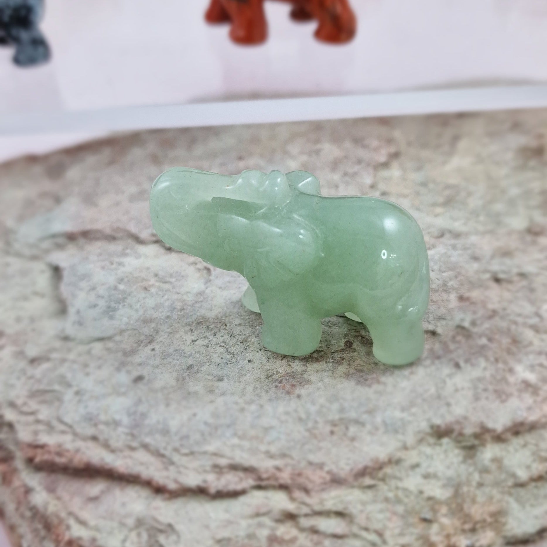 Small Green Aventurine elephant on a rock with other crystal elephants in the background