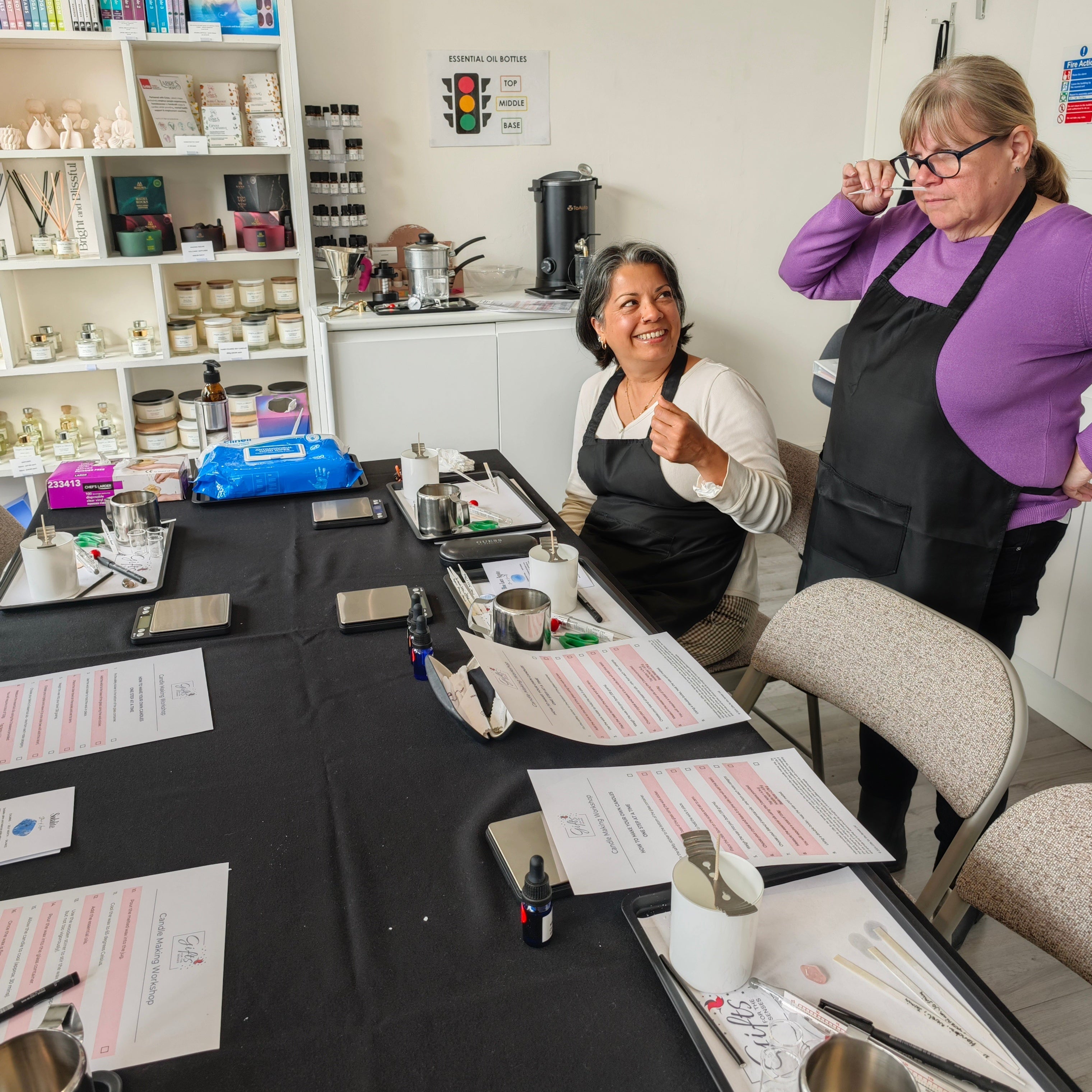 Two women in a workshop setting with tools and materials on a table.