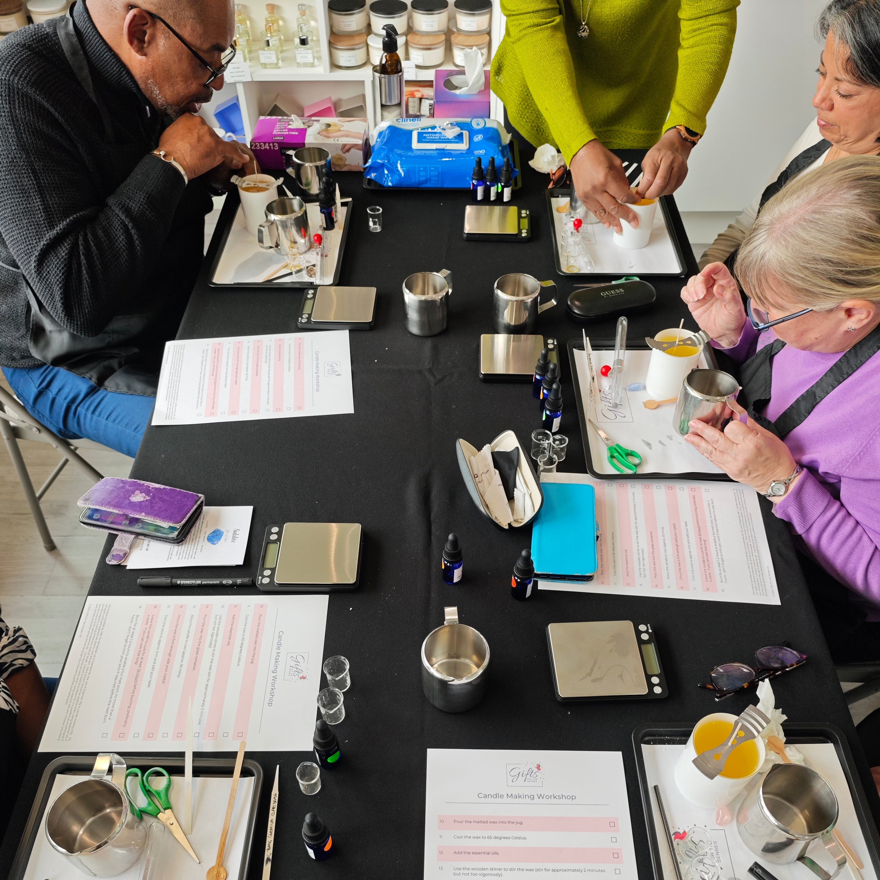Group of people at a table with various items including papers, cups, and tools.