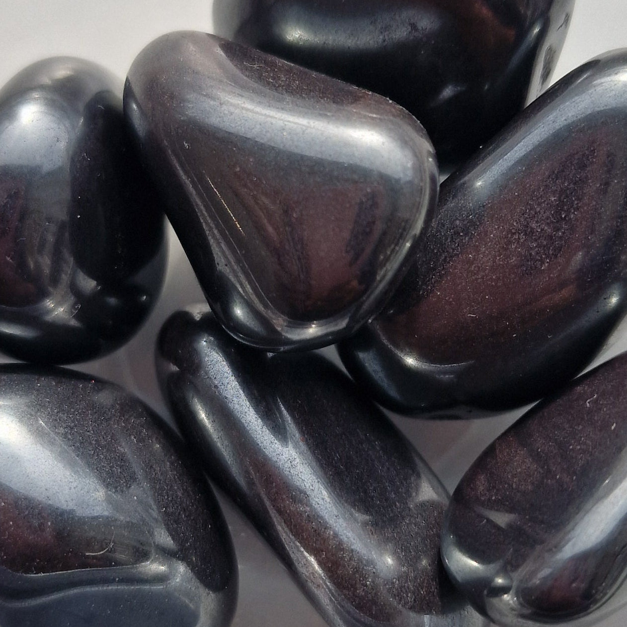 Black hematite stones in a clear glass bowl on a light gray background