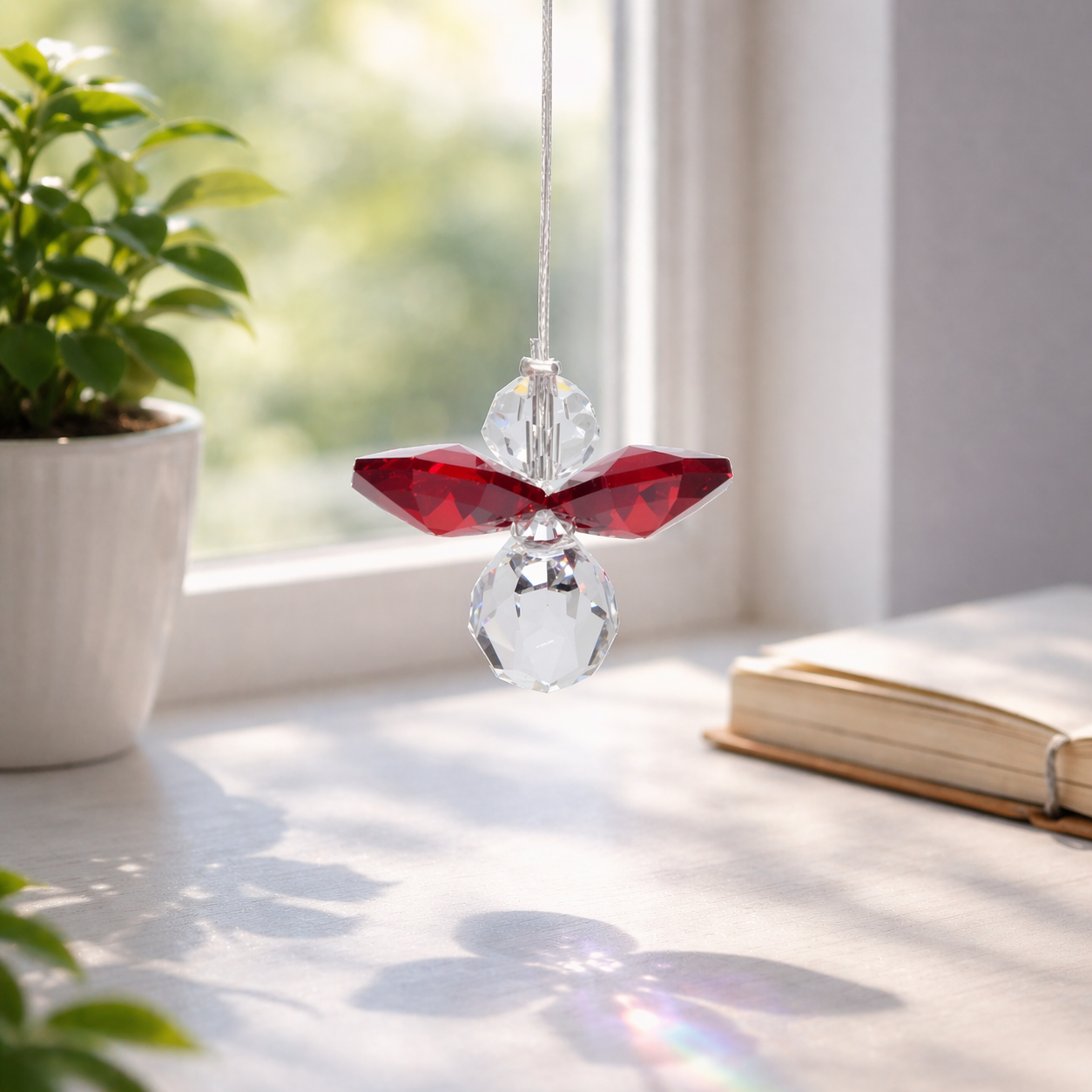 Colorful crystal angel decoration hanging on a wire with a plant and book in the background.