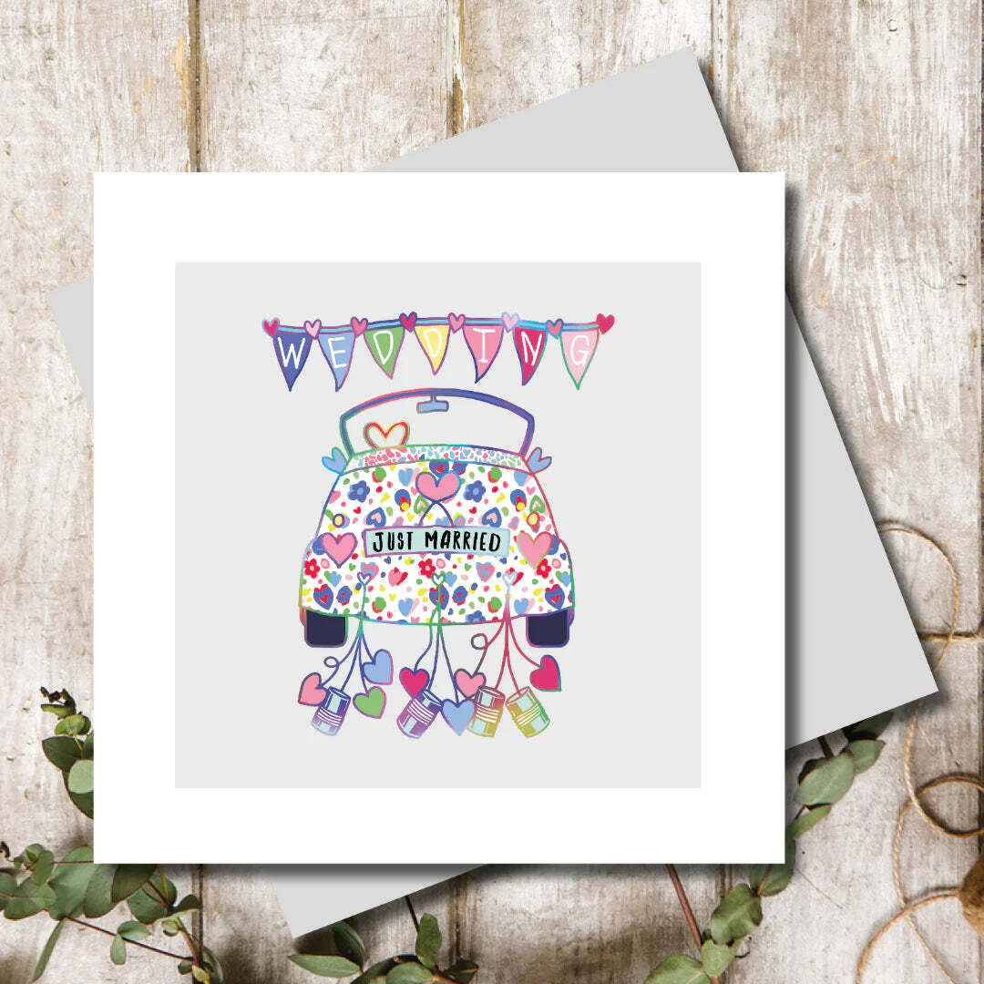 Greeting card with a decorated car illustration and 'Just Married' text on a wooden surface.