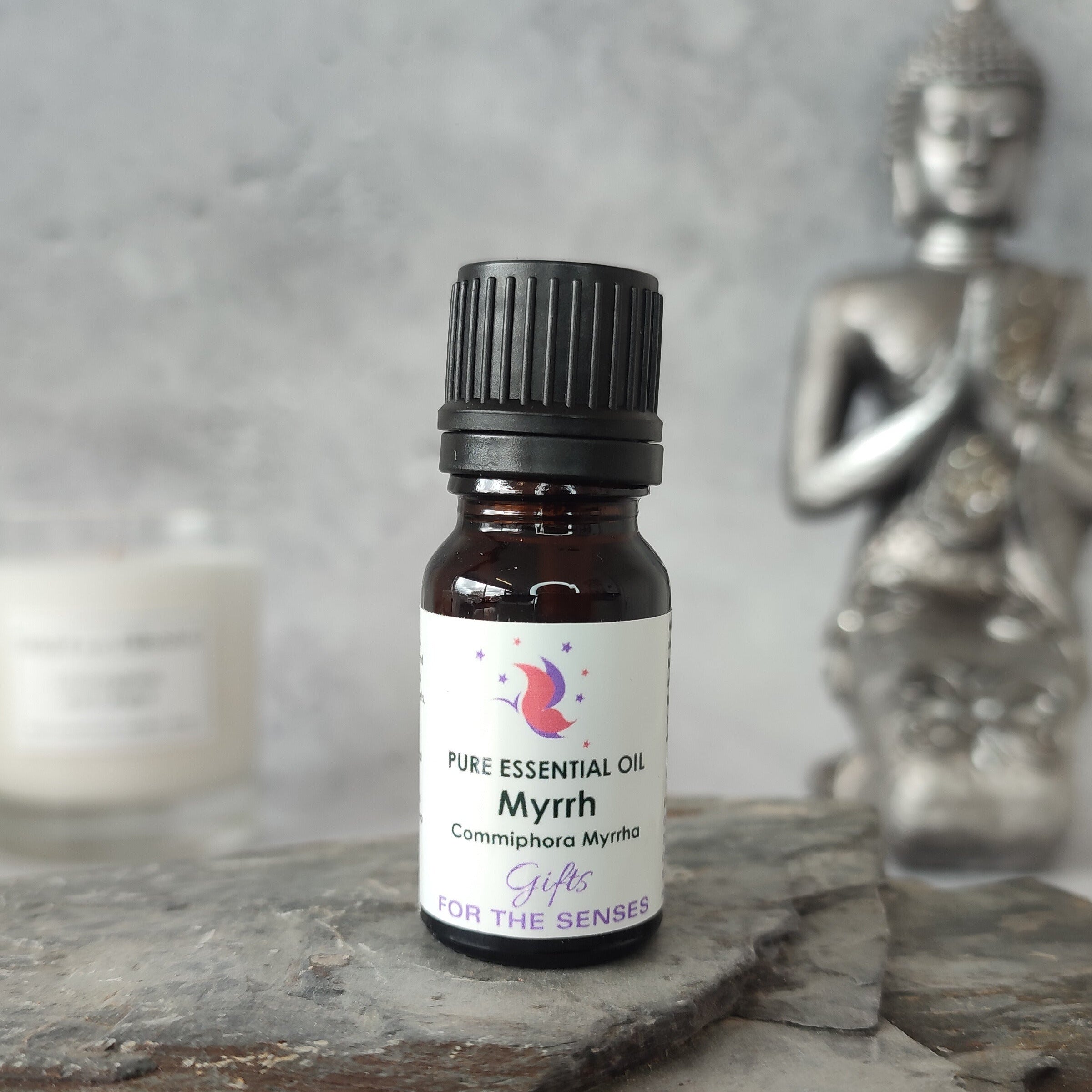 Bottle of pure essential oil labeled 'Myrrh' on a stone surface with a Buddha statue in the background.