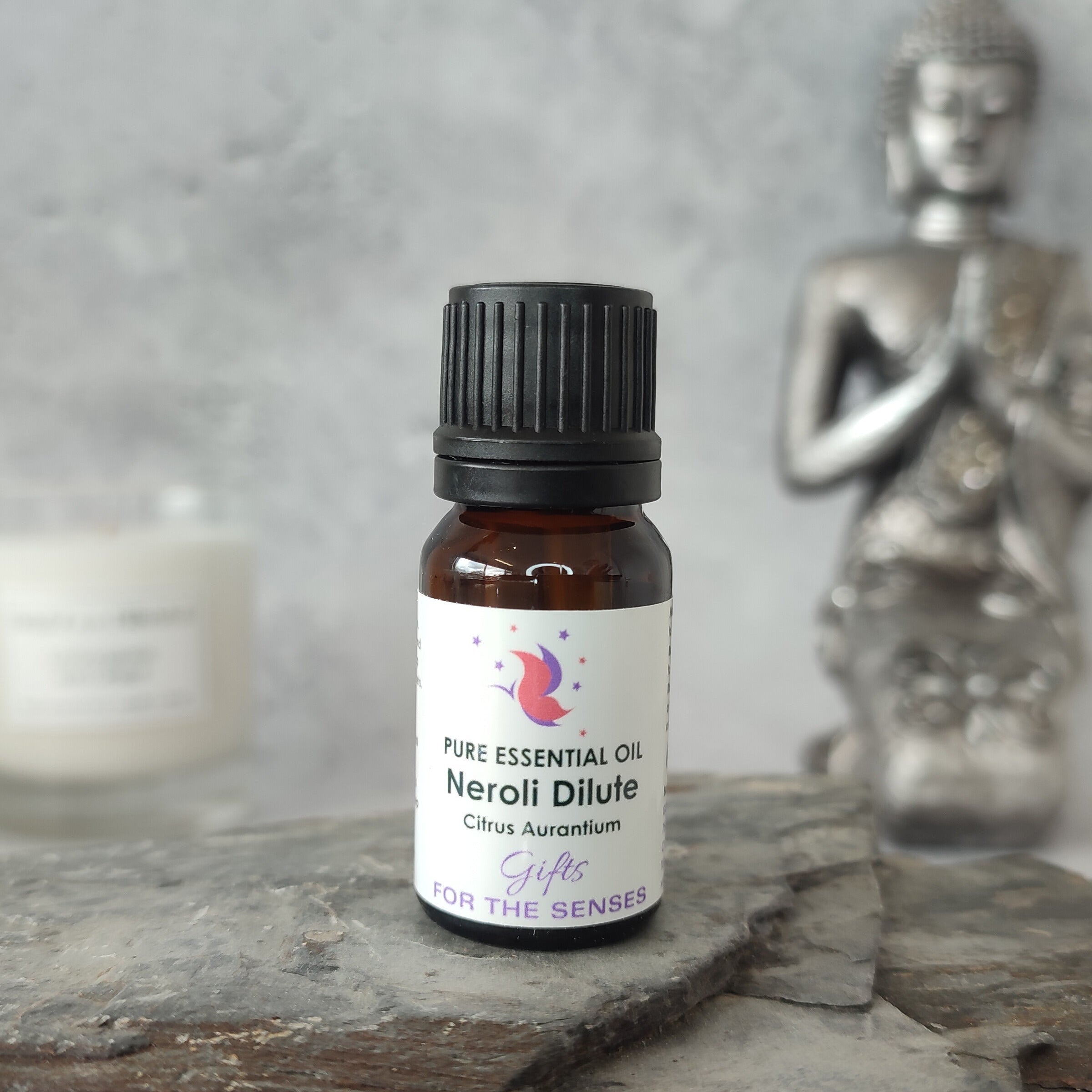Bottle of Pure Essential Oil Neroli Dilute on a stone surface with a Buddha statue in the background.