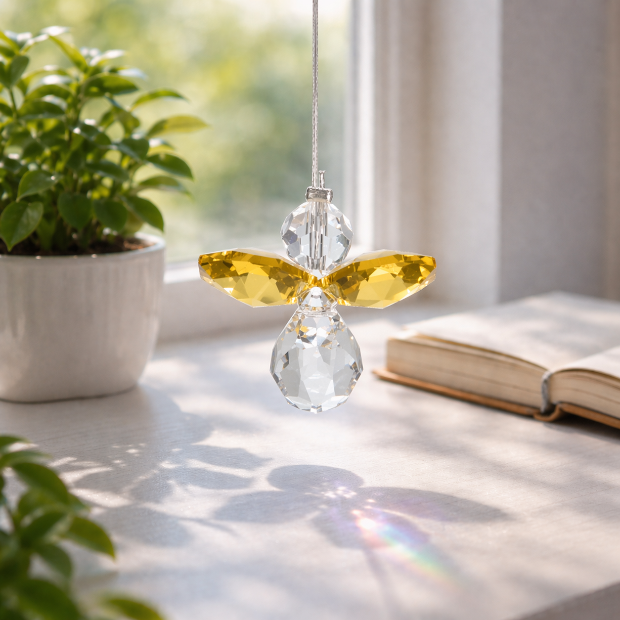 Crystal angel hanging ornament on a windowsill with plants and a book in the background