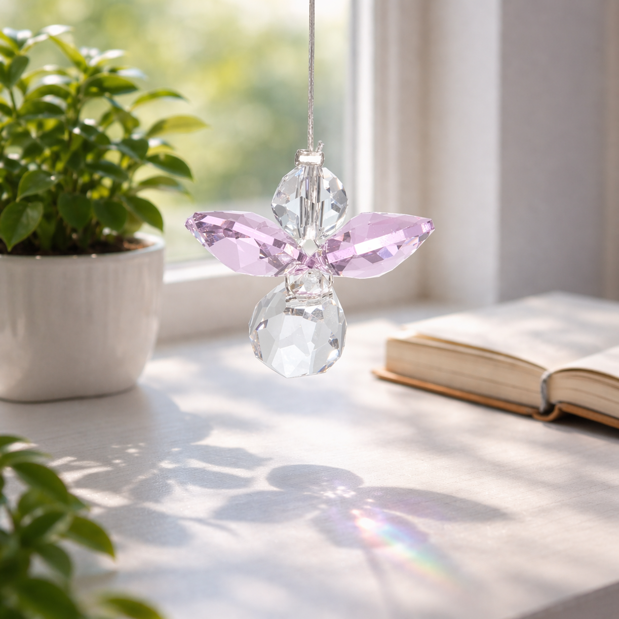 Crystal angel ornament on a windowsill with plants and a book in the background