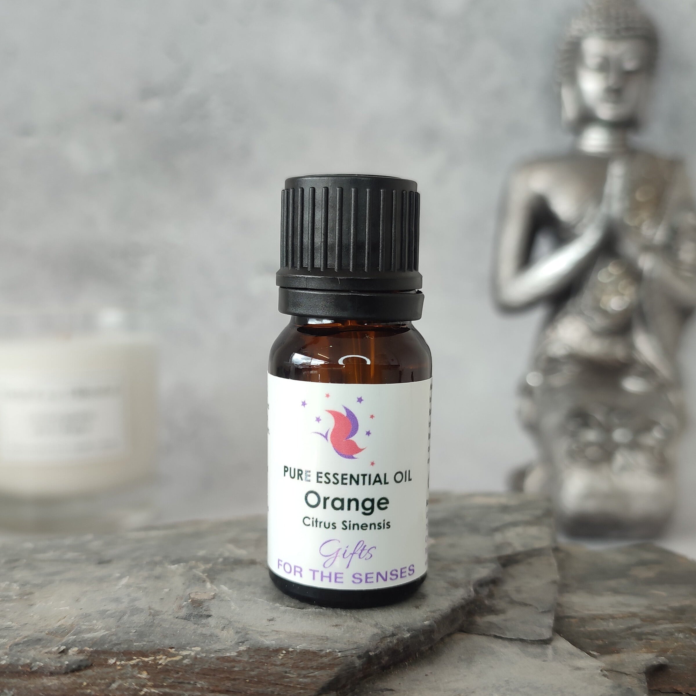Orange essential oil bottle on a stone surface with a Buddha statue in the background